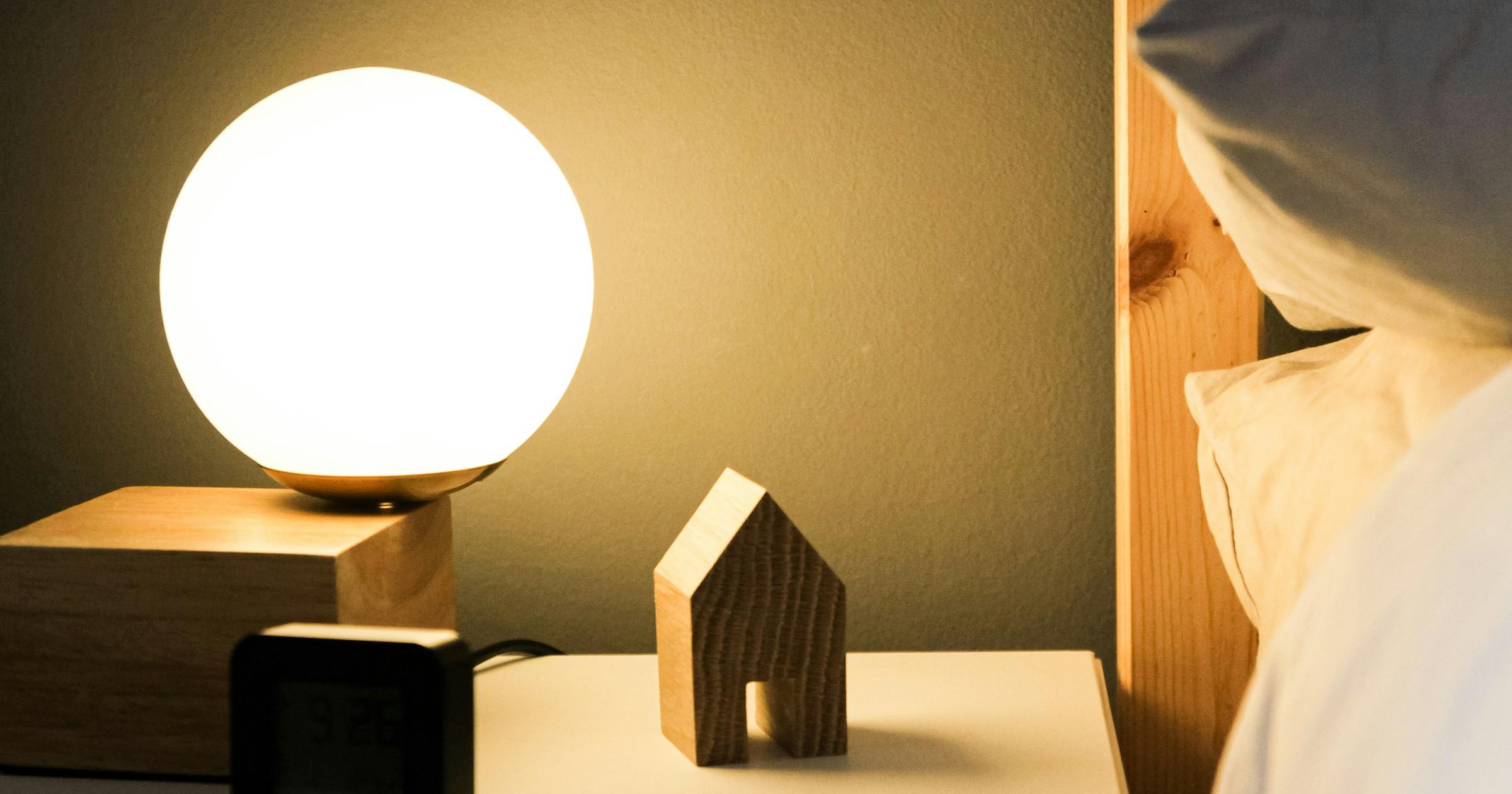 Softly glowing globe lamp, small wooden house and digital clock on a bedside nightstand at night