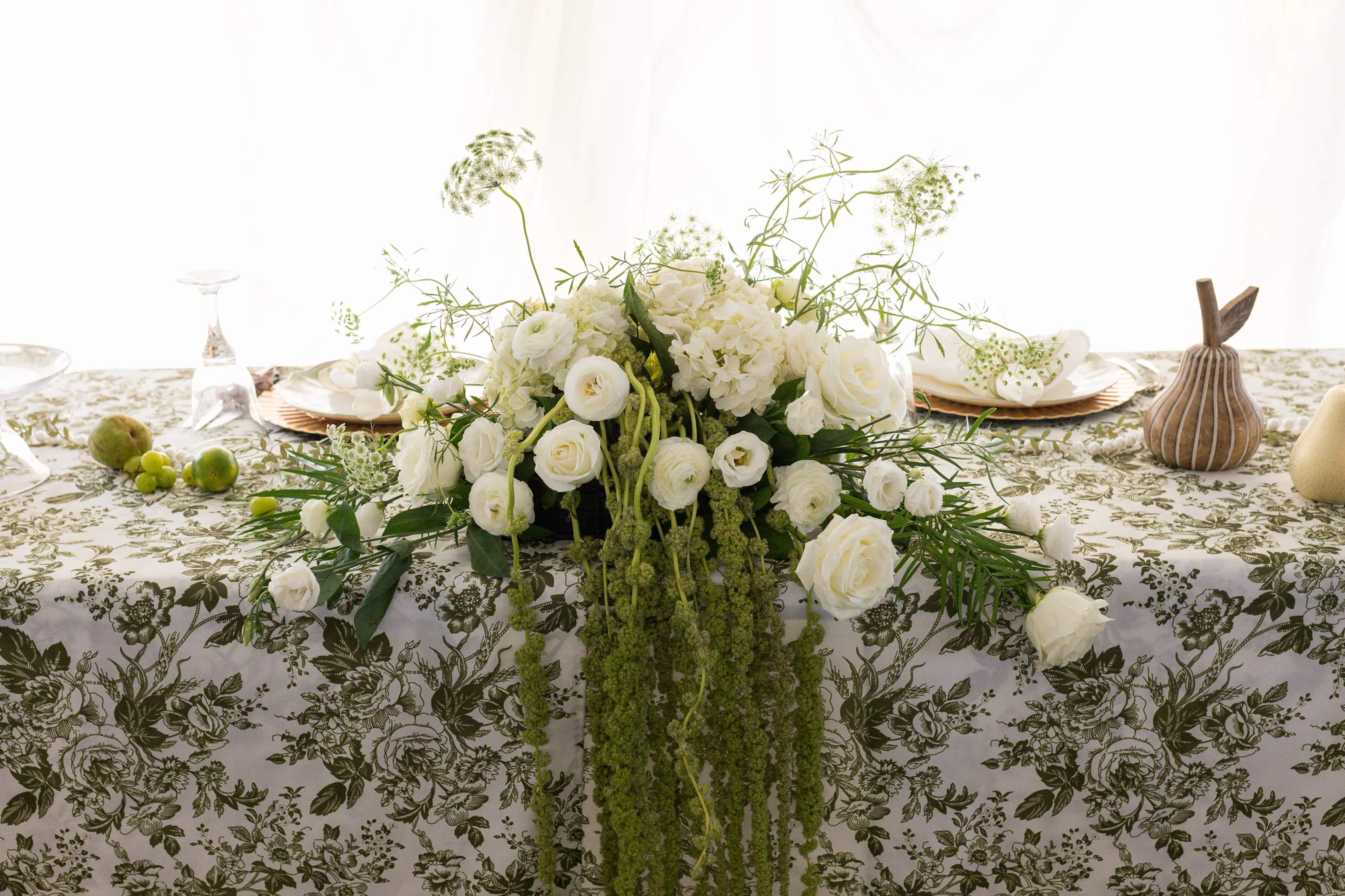 Low sweetheart-table arrangement of white hydrangea, garden roses and ranunculus with Queen Anne's lace and a cascade of green amaranthus over a green toile cloth