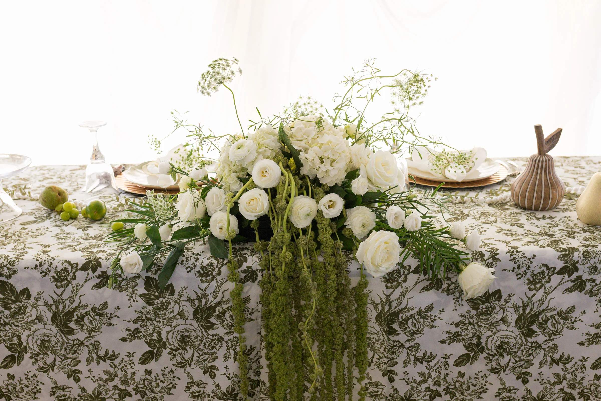 Low sweetheart-table arrangement of white hydrangea, garden roses and ranunculus with Queen Anne's lace and a cascade of green amaranthus over a green toile cloth