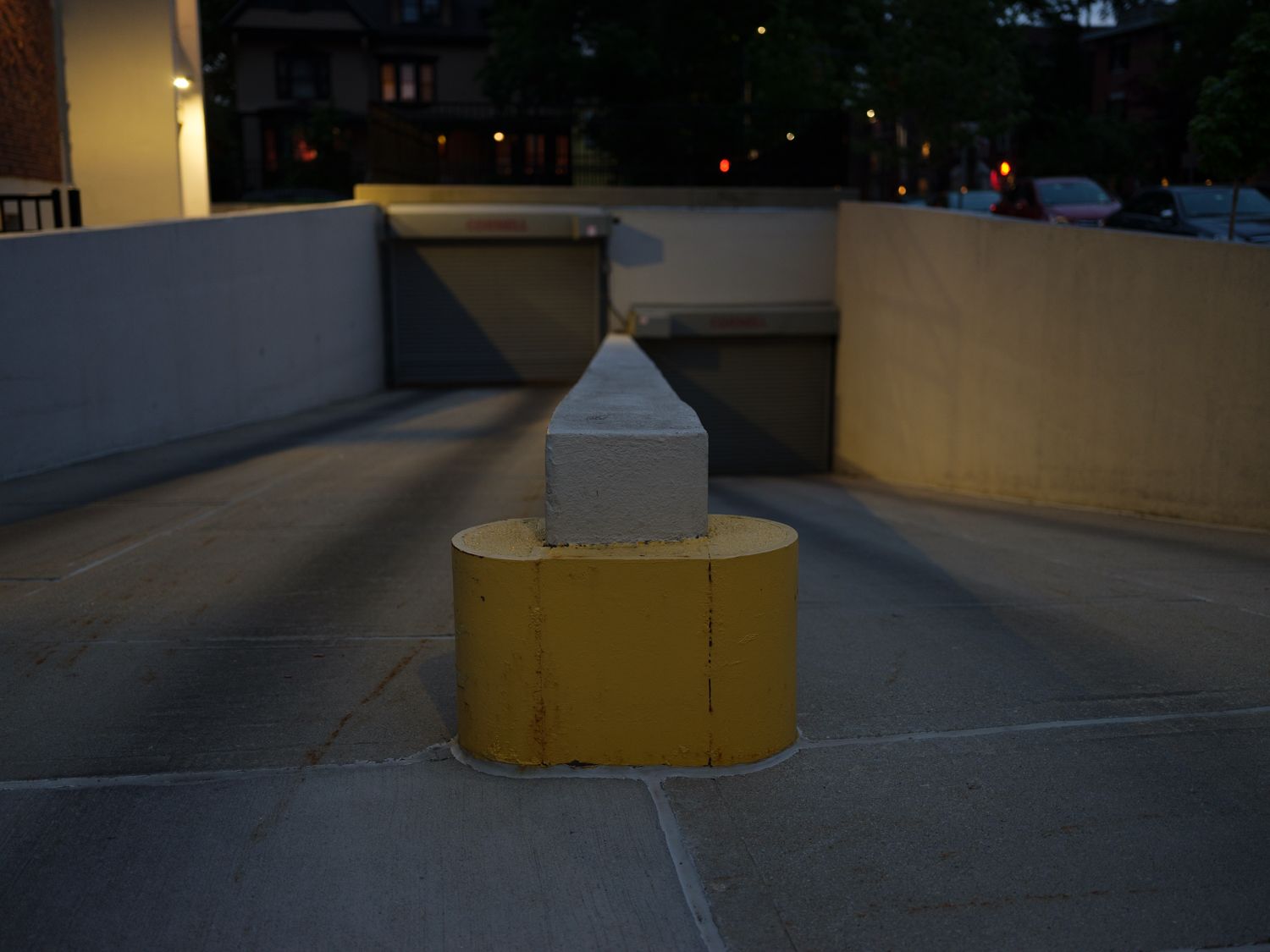 A photograph of a parking garage entrance, the barrier between the entrance and exit is yellow and centered in the frame, it is night time so the lights cast shadows around the image