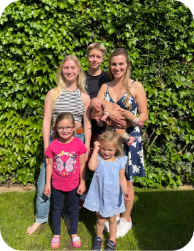 Fünf Personen die nebeneinander stehen an einem Sommertag. Eine Person hält ein Baby im Arm.
