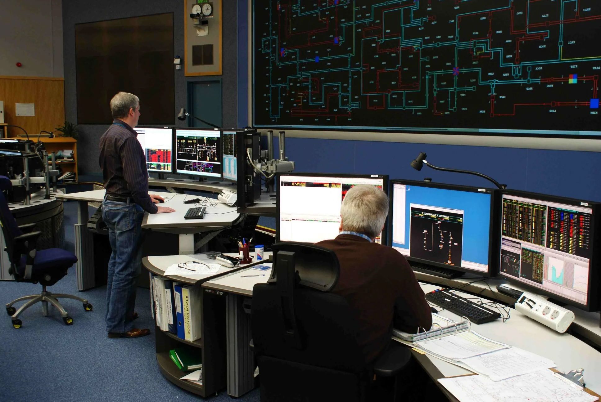 Control room operators monitoring complex process systems through multiple HMI displays, illustrating professional interface design as cognitive infrastructure for decision making