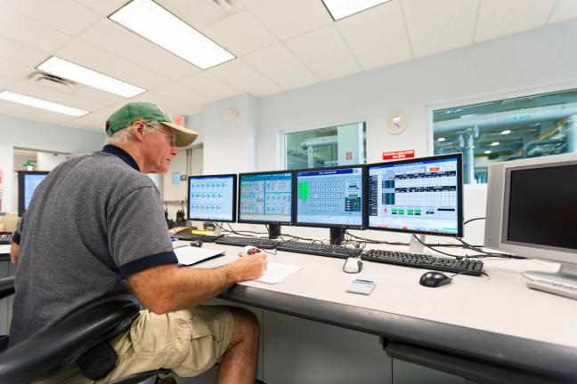 Industrial operator monitoring process control systems through multiple HMI displays, illustrating usability renewal and alignment between human and machine