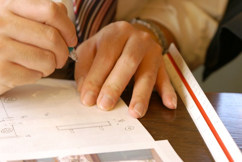 三角スケールを当てて図面に描き込んでいる設計者の手元
