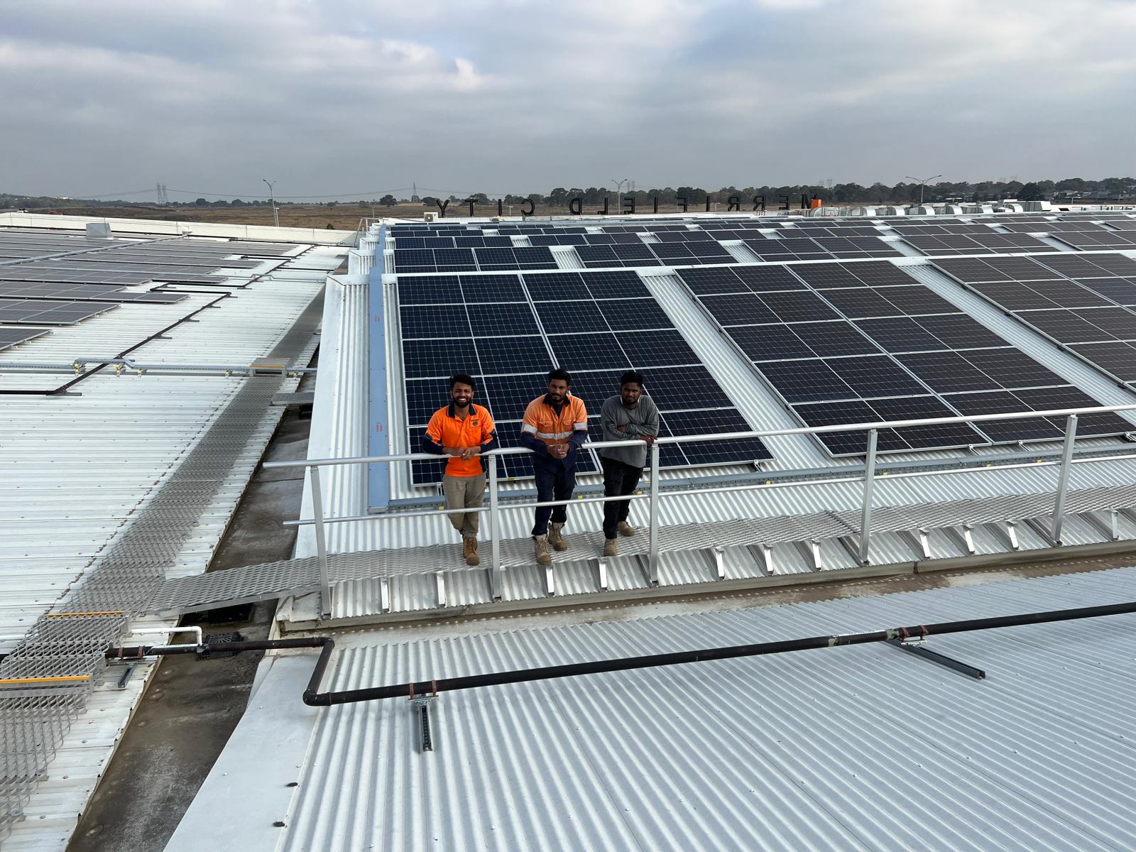 Three JM Solar installers standing by a large commercial rooftop solar array at Merrifield