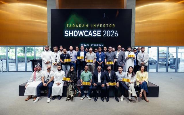 A large group of founders and mentors from TAQADAM Cohort 9 pose together on stage under a screen reading "TAQADAM Investor Showcase 2026" at KAUST.