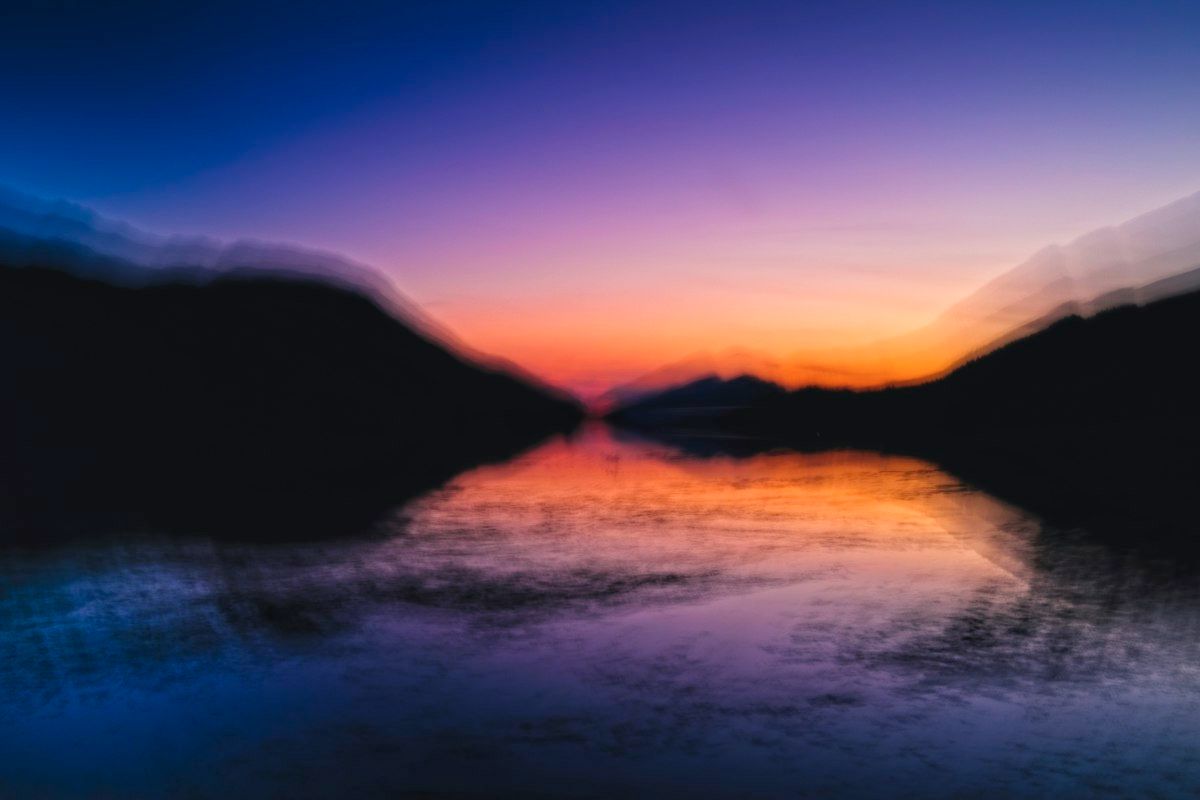 Blurred sunset glowing over a lake between dark hills