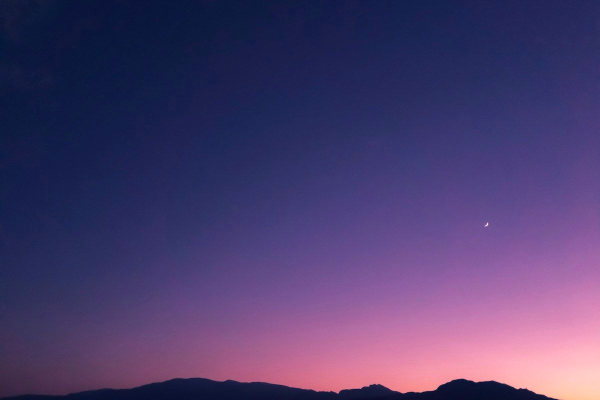 Purple dusk sky with a crescent moon over distant hills
