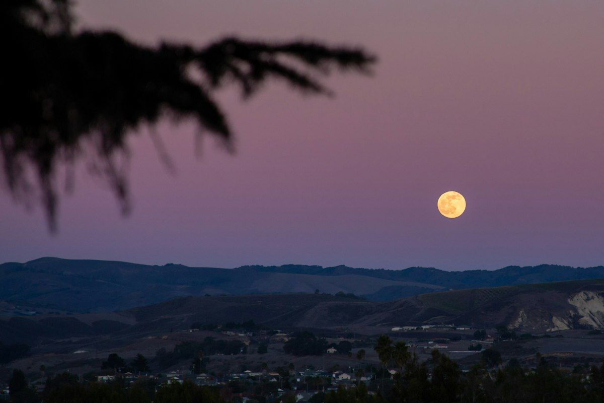 Full moon rising over a darkened hillside at dusk