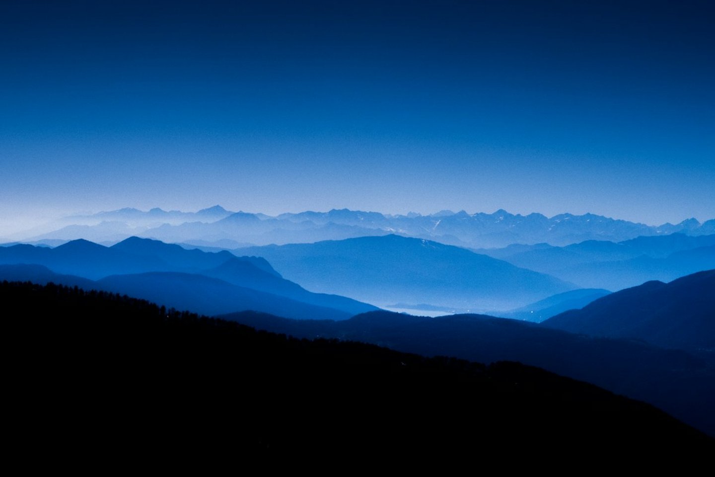 Layered blue mountain silhouettes under a deep blue sky