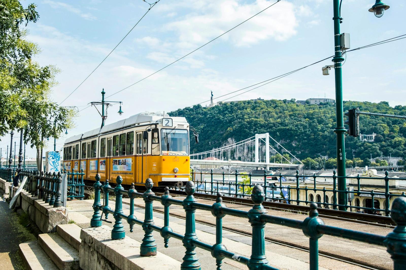 Klasszikus sárga villamos a budapesti Duna-parton, a Gellért-heggyel és az Erzsébet híddal a háttérben