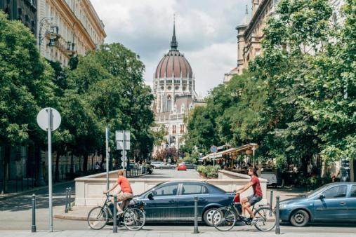 A tree-lined Budapest street of classic apartment buildings, with the Parliament dome in the distance