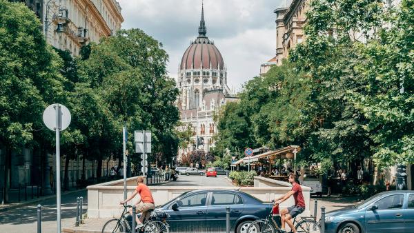 A tree-lined Budapest street of classic apartment buildings, with the Parliament dome in the distance