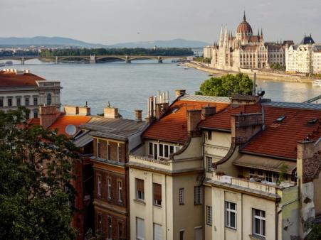 Rooftops of central Budapest apartment buildings above the Danube, with the Parliament and Margaret Bridge beyond