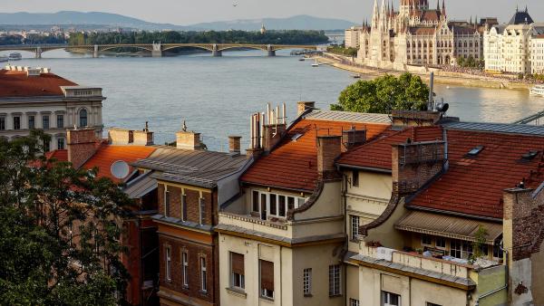 Rooftops of central Budapest apartment buildings above the Danube, with the Parliament and Margaret Bridge beyond