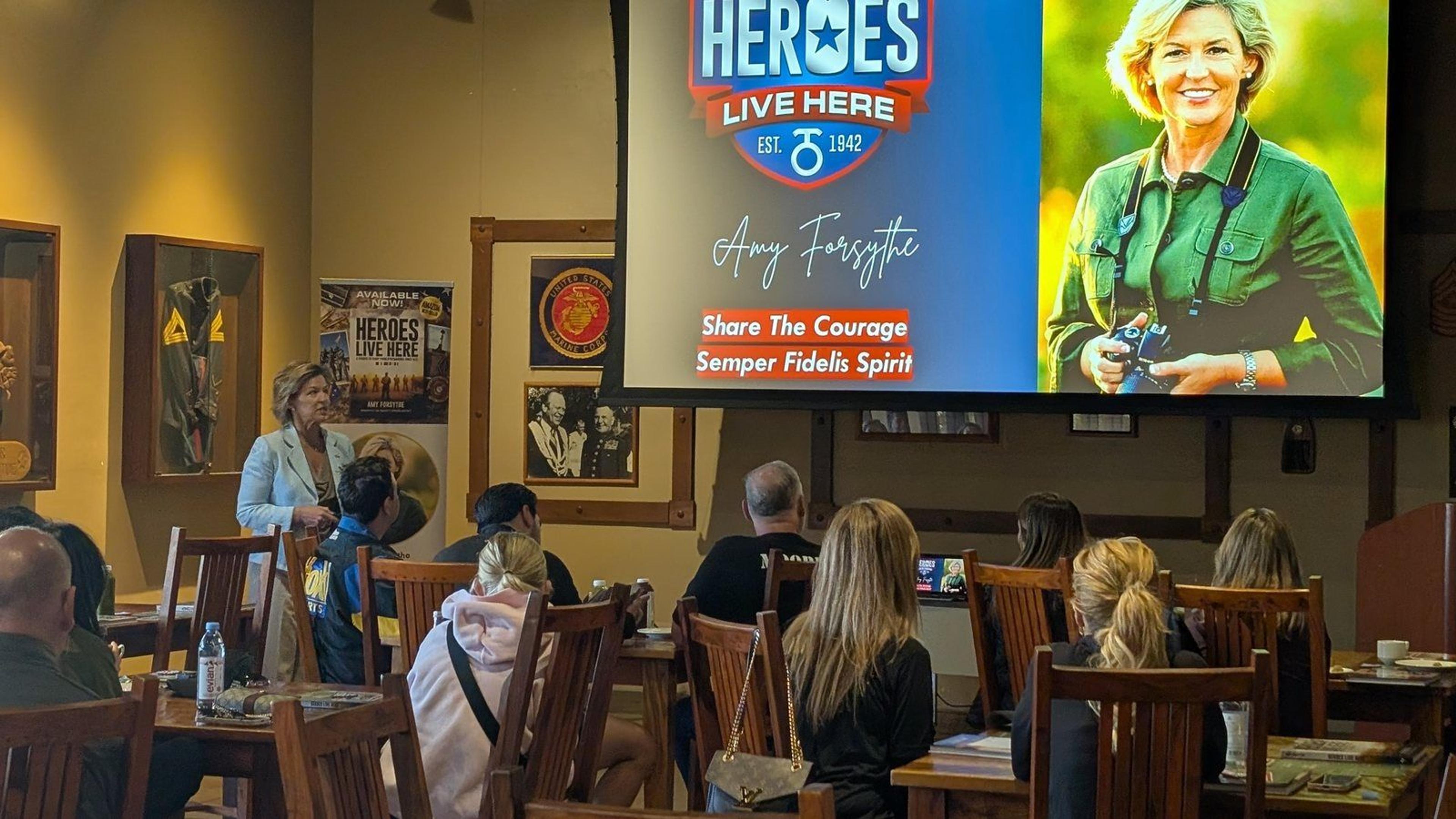 Amy Forsythe speaking to seated guests beside a presentation about Camp Pendleton