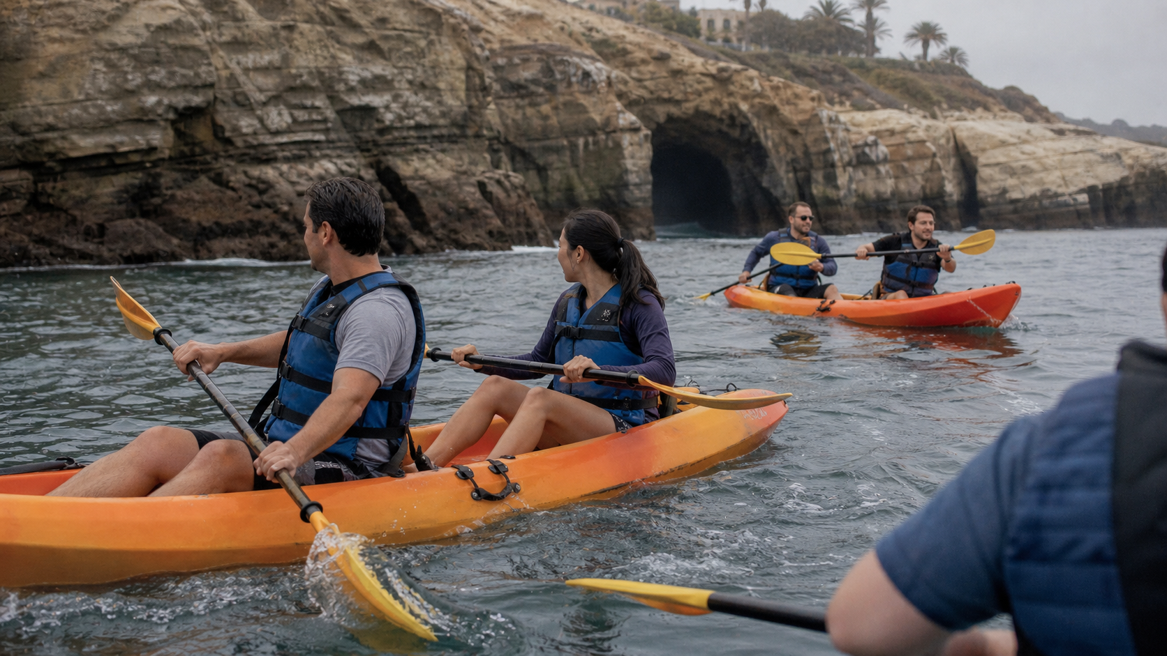 Adult coworkers paddle tandem kayaks near the La Jolla sea caves