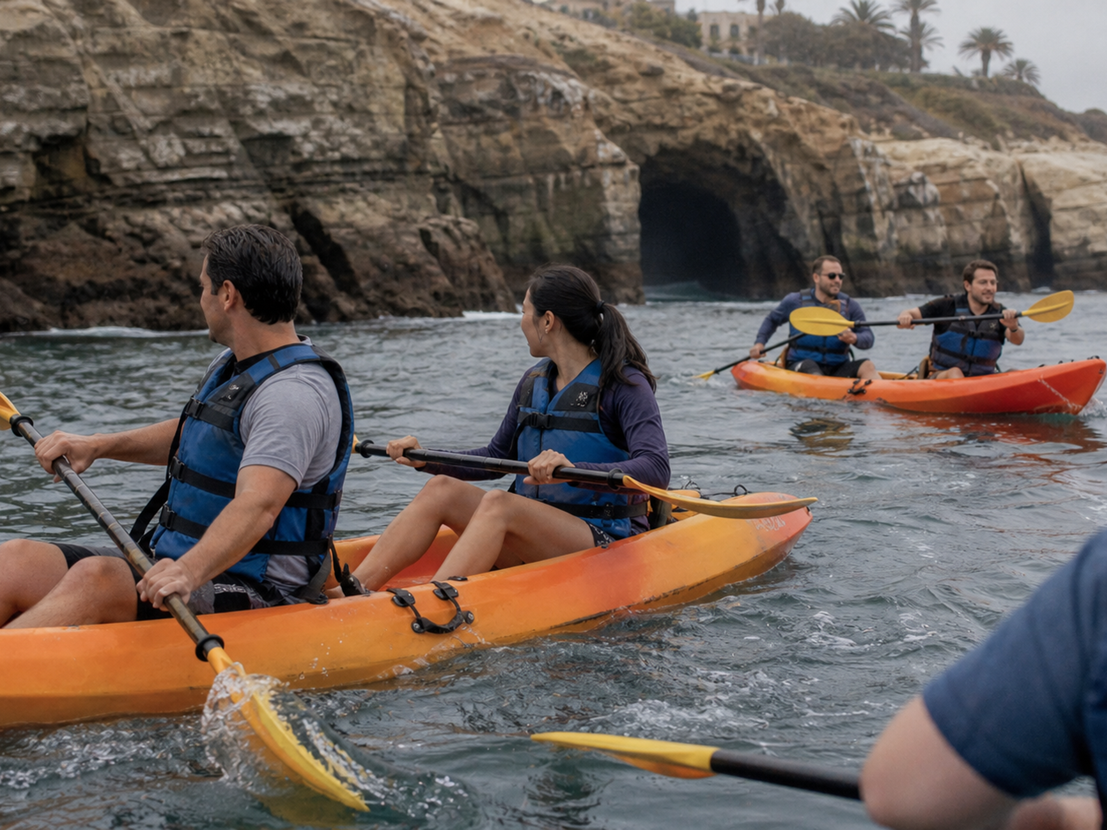 Adult coworkers paddle tandem kayaks near the La Jolla sea caves
