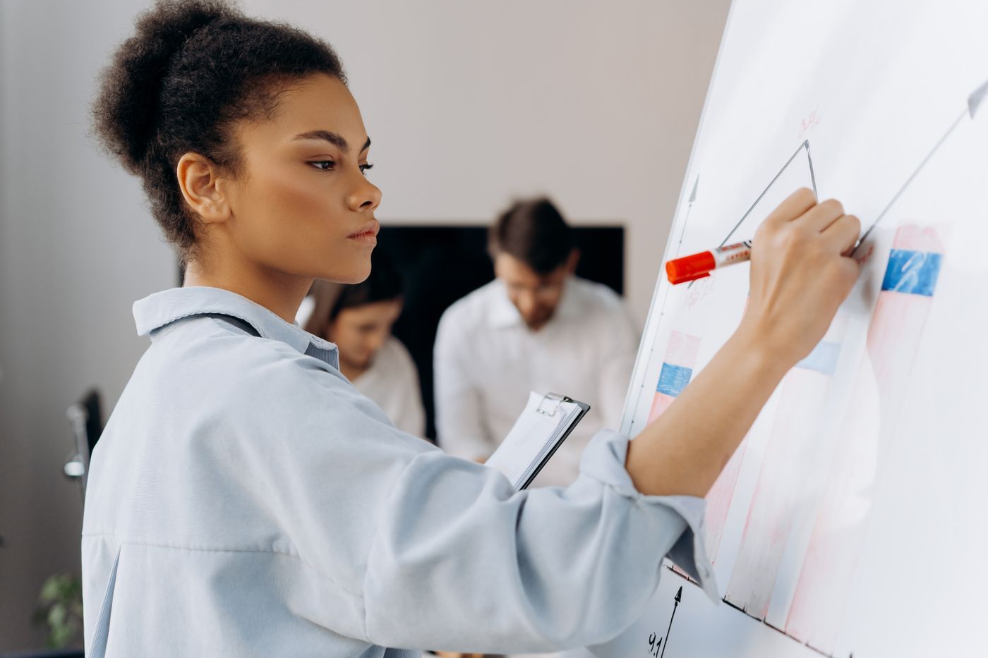 A colleague leading a discussion at a whiteboard while teammates listen