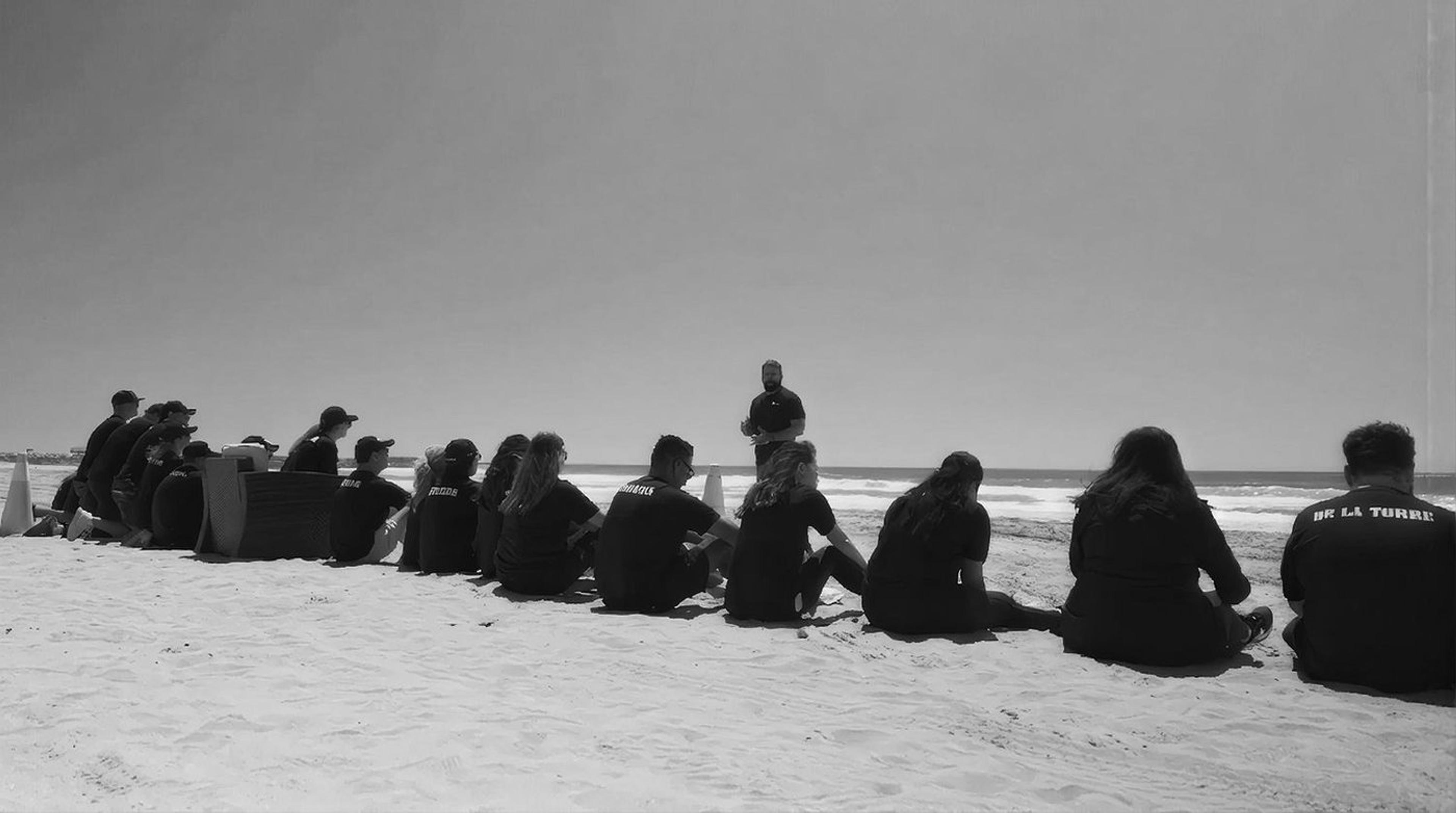 A group seated on the sand listening to an instructor beside the Pacific at Camp Pendleton