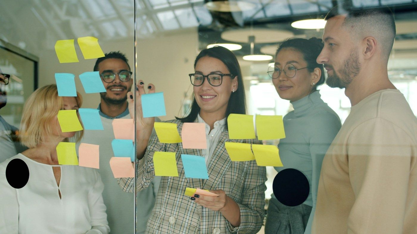 Colleagues sharing ideas using sticky notes on a glass board