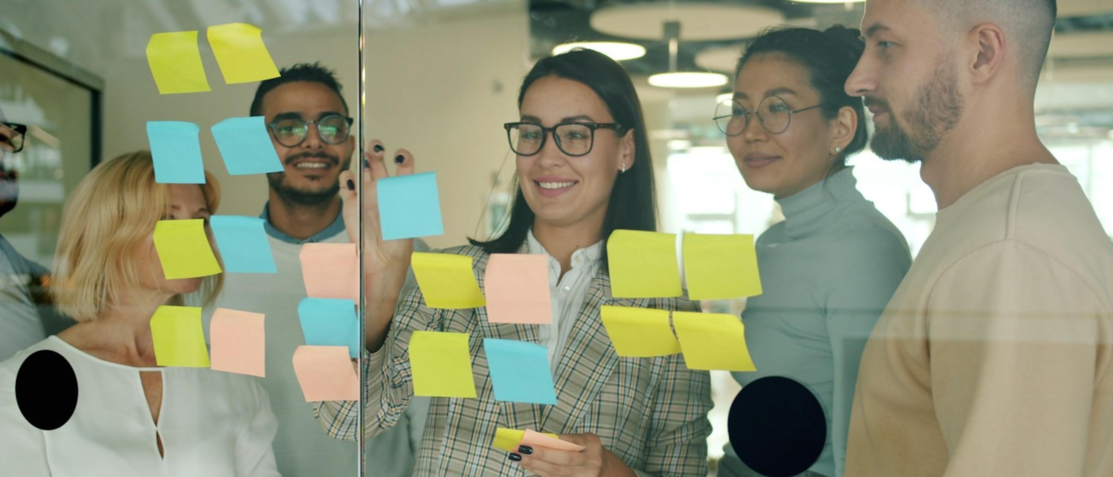 Colleagues sharing ideas using sticky notes on a glass board