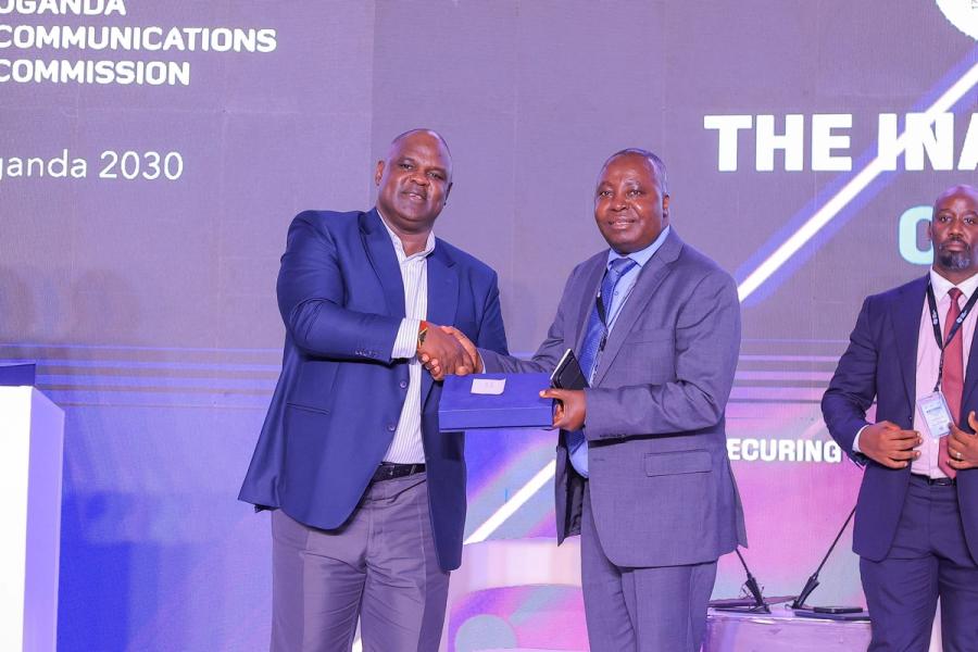 Airtel Money Commerce Uganda Limited (AMCUL) Managing Director Japhet Aritho receives a plaque from Joseph Kizito, Head of Consumer Affairs, UCC, during day 1 of the inaugural National Cybersecurity Conference in Kampala.