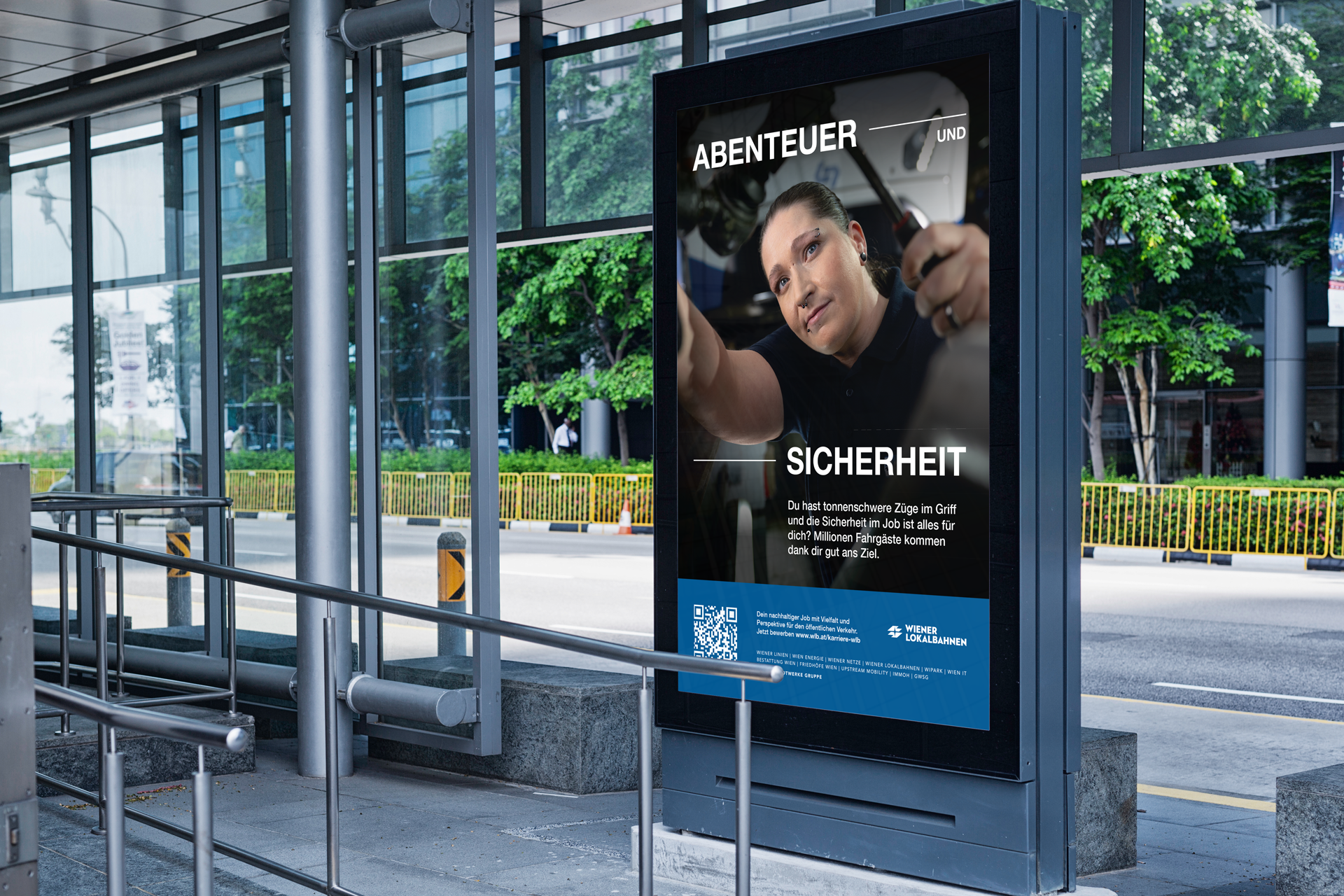 Das Bild zeigt ein Werbeplakat an einer Bushaltestelle in einer städtischen Umgebung. Im Hintergrund sind Glasfenster und eine Straße mit grünen Bäumen und Büschen zu sehen. Auf dem Plakat ist eine Frau abgebildet, die konzentriert an einem Zug arbeitet. Über ihr steht der Text „ABENTEUER UND SICHERHEIT“. Darunter steht: „Du hast tonnenschwere Züge im Griff und die Sicherheit im Job ist alles für dich? Millionen Fahrgäste kommen dank dir gut ans Ziel.“. Unten auf dem Plakat befinden sich ein QR-Code und das Logo der „WIENER LOKALBAHNEN“.