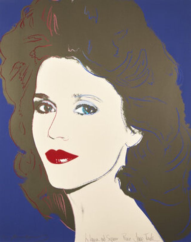 A pop-art style screenprint portrait of a woman against a solid blue background. She has voluminous, curly brown hair with dark red highlights, pale skin rendered in bold outline, blue eyes, arched eyebrows, and bright red lips. Cursive handwritten text is visible near the bottom of the image.