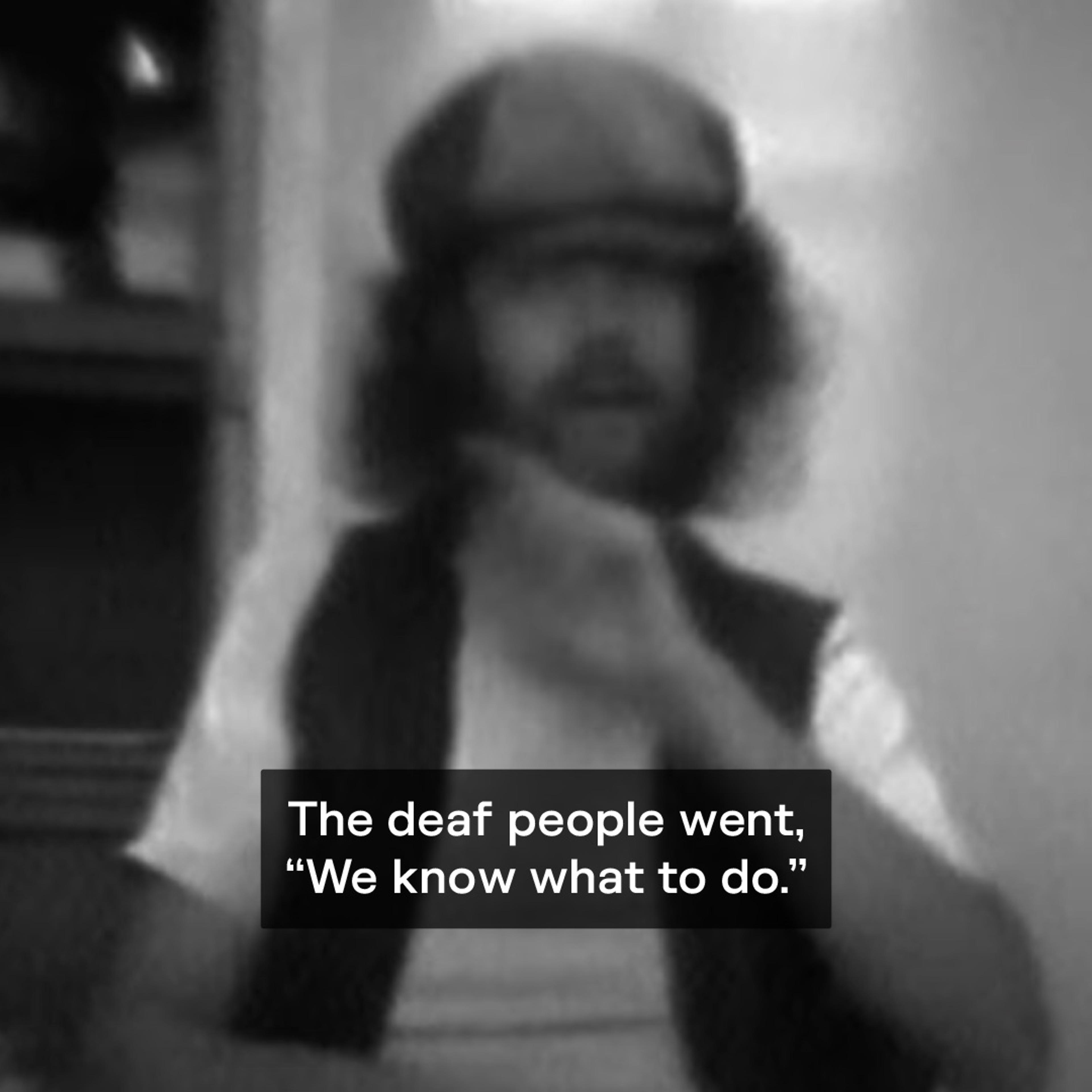 Black-and-white still of a man signing, captioned “The deaf people went, ‘We know what to do.’”