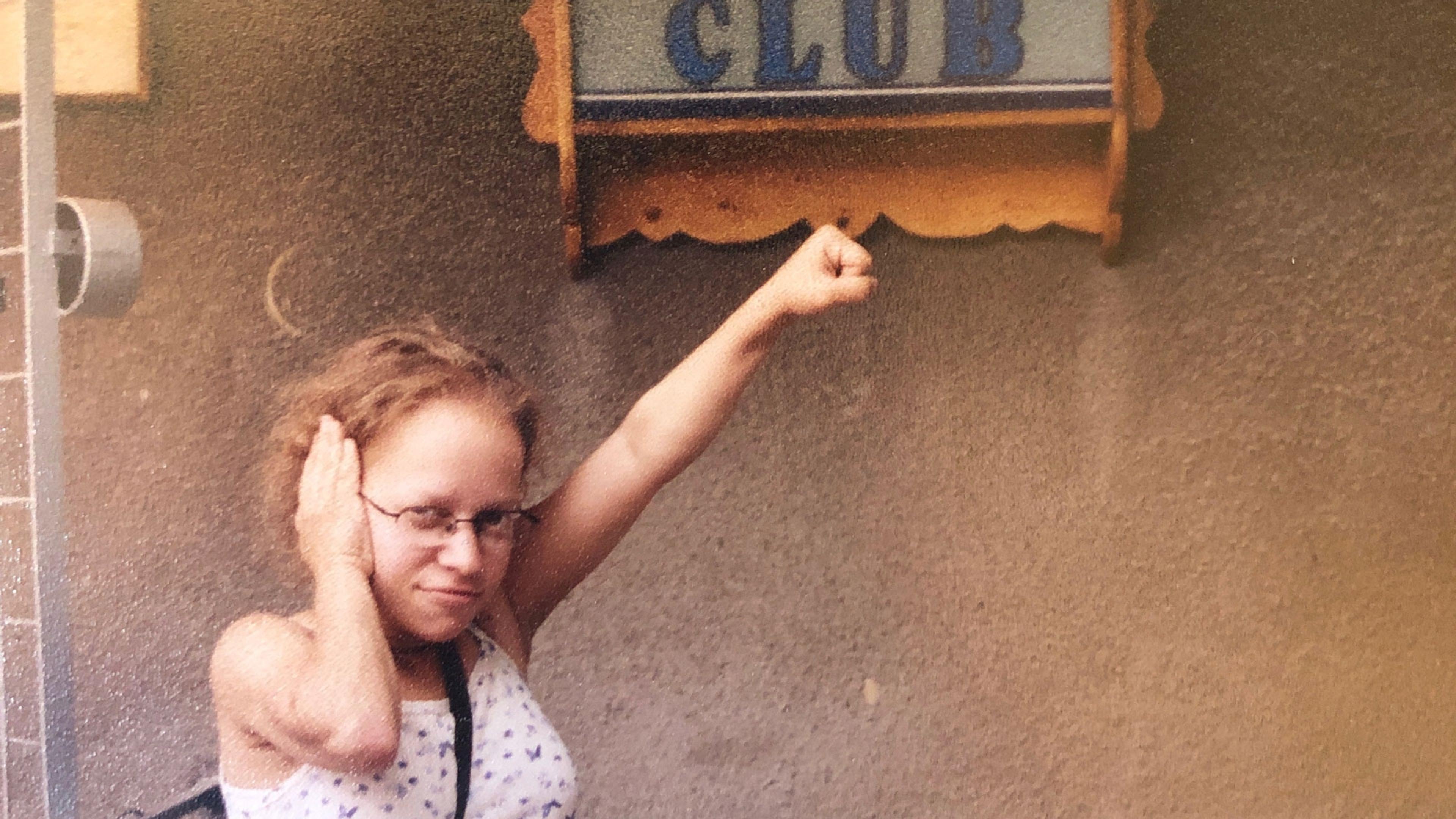 A woman under a “Club” sign making the Deaf Power sign