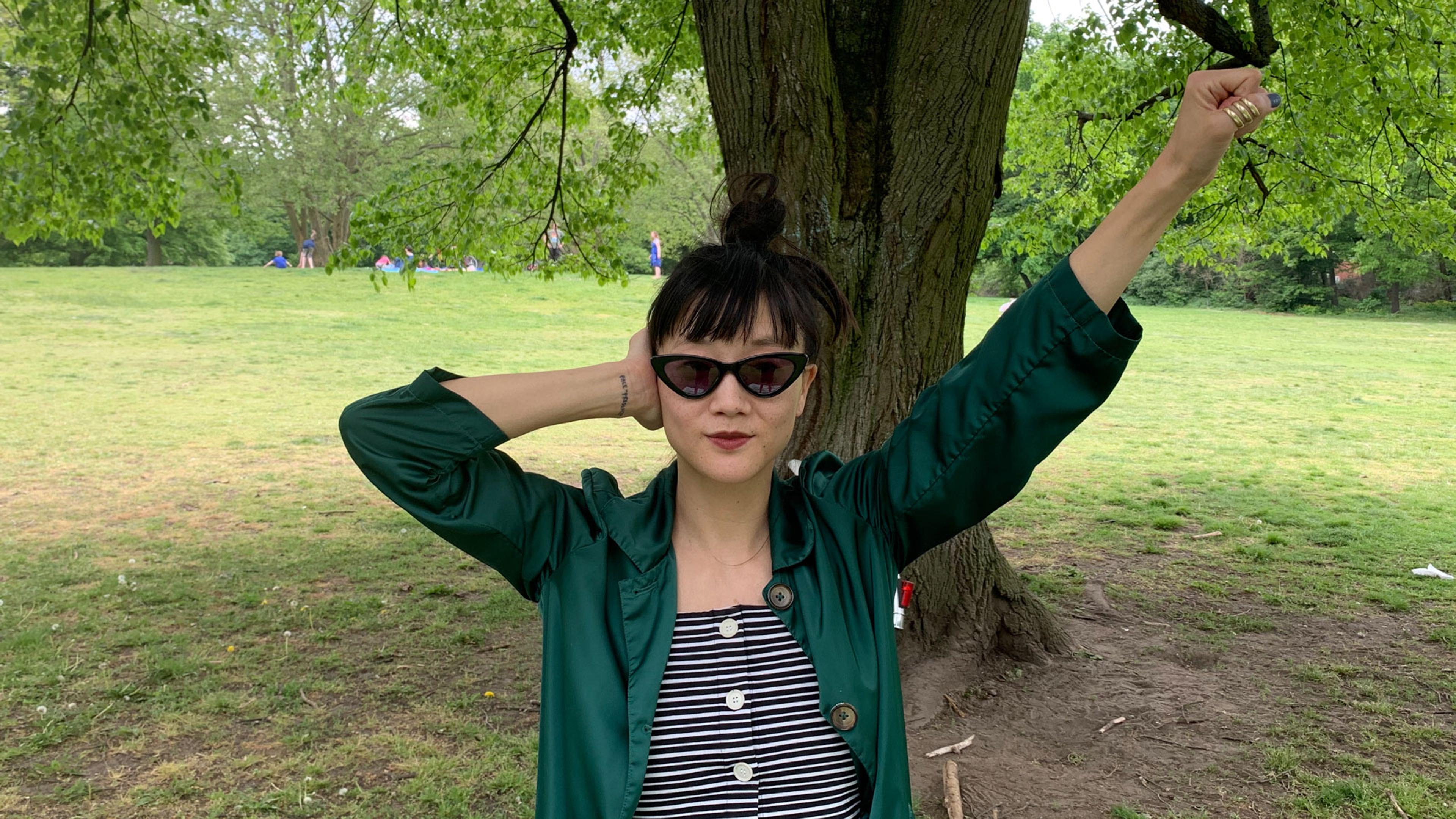 A woman in sunglasses in a park making the Deaf Power sign