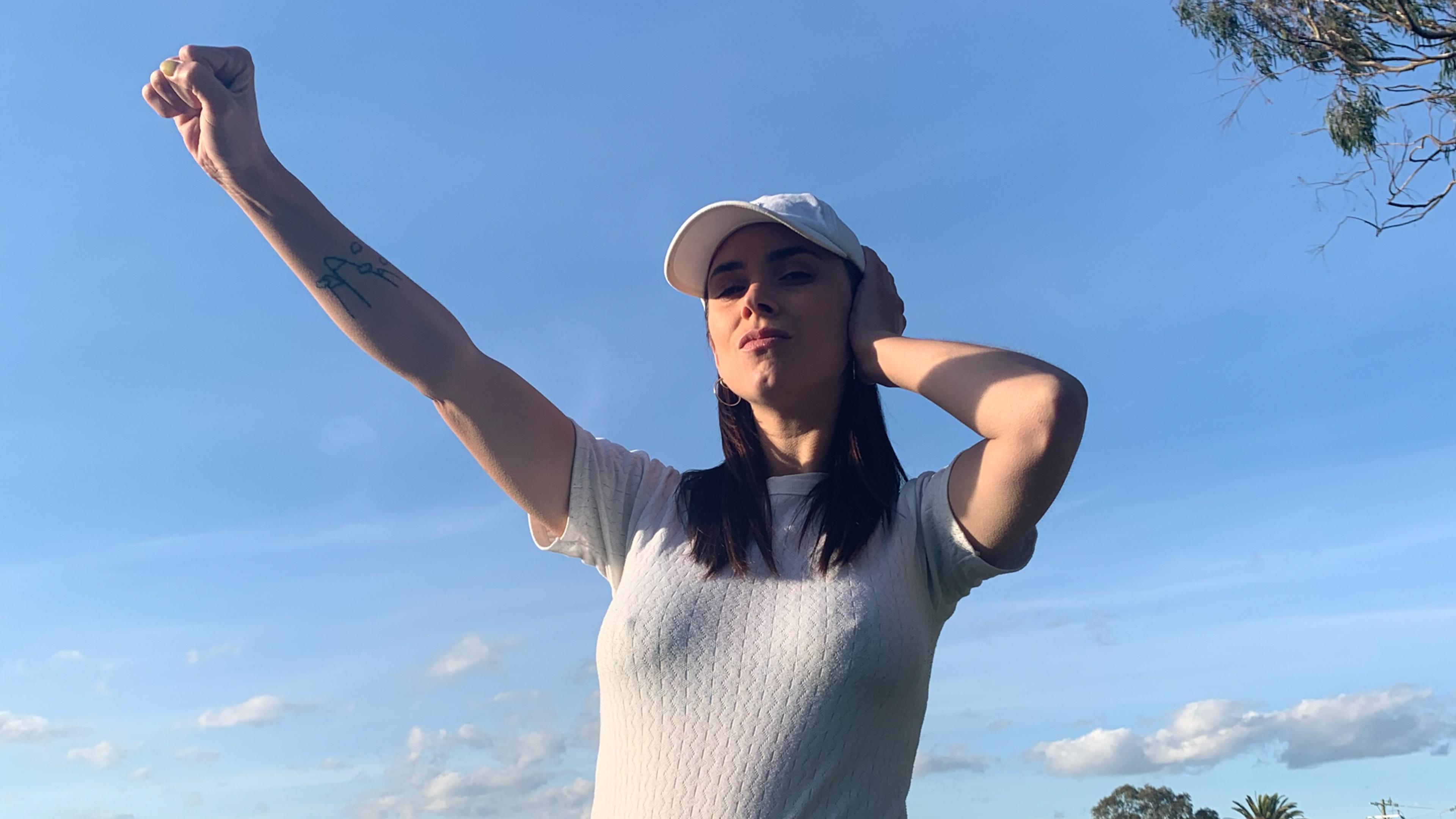 A woman in a cap against a blue sky making the Deaf Power sign