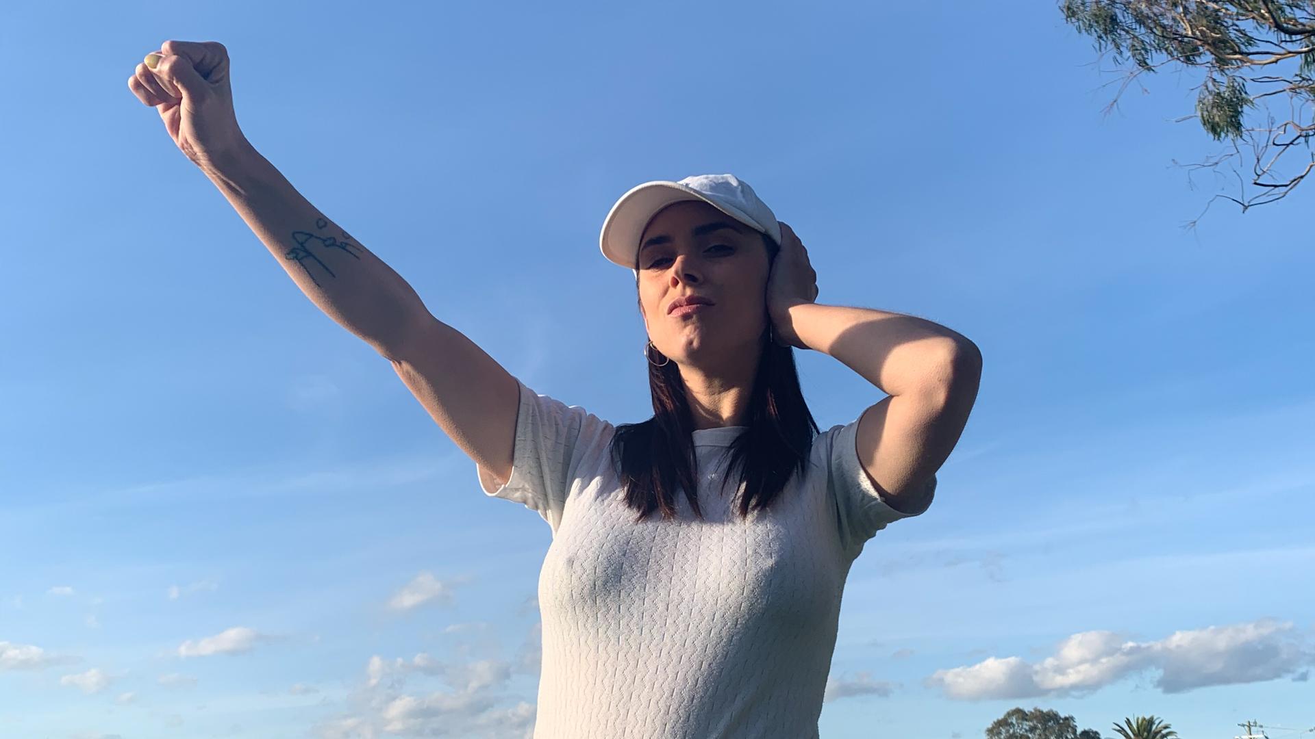 A woman in a cap against a blue sky making the Deaf Power sign