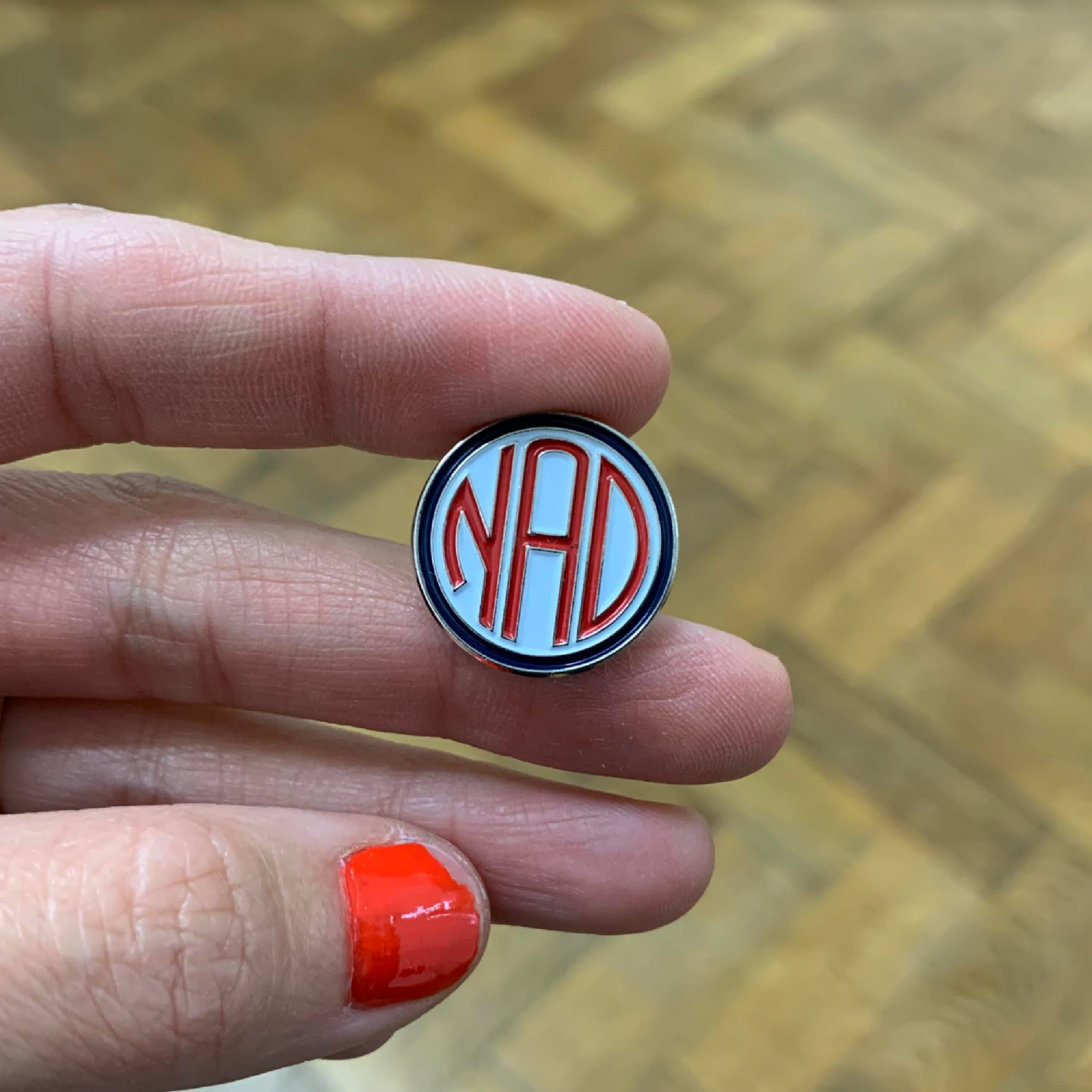 A hand holding an enamel NAD pin
