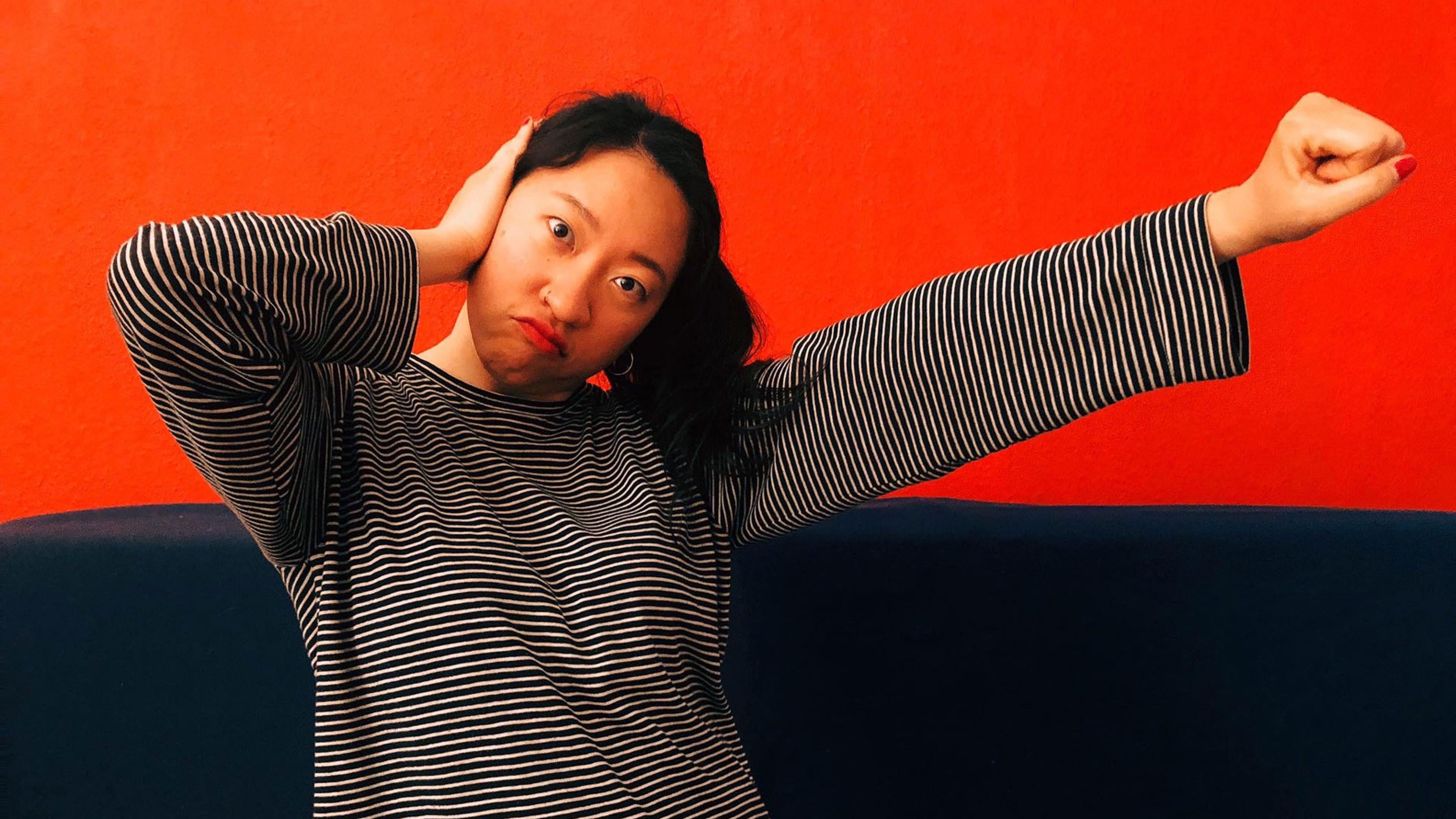 A woman in a striped top against a red wall making the Deaf Power sign