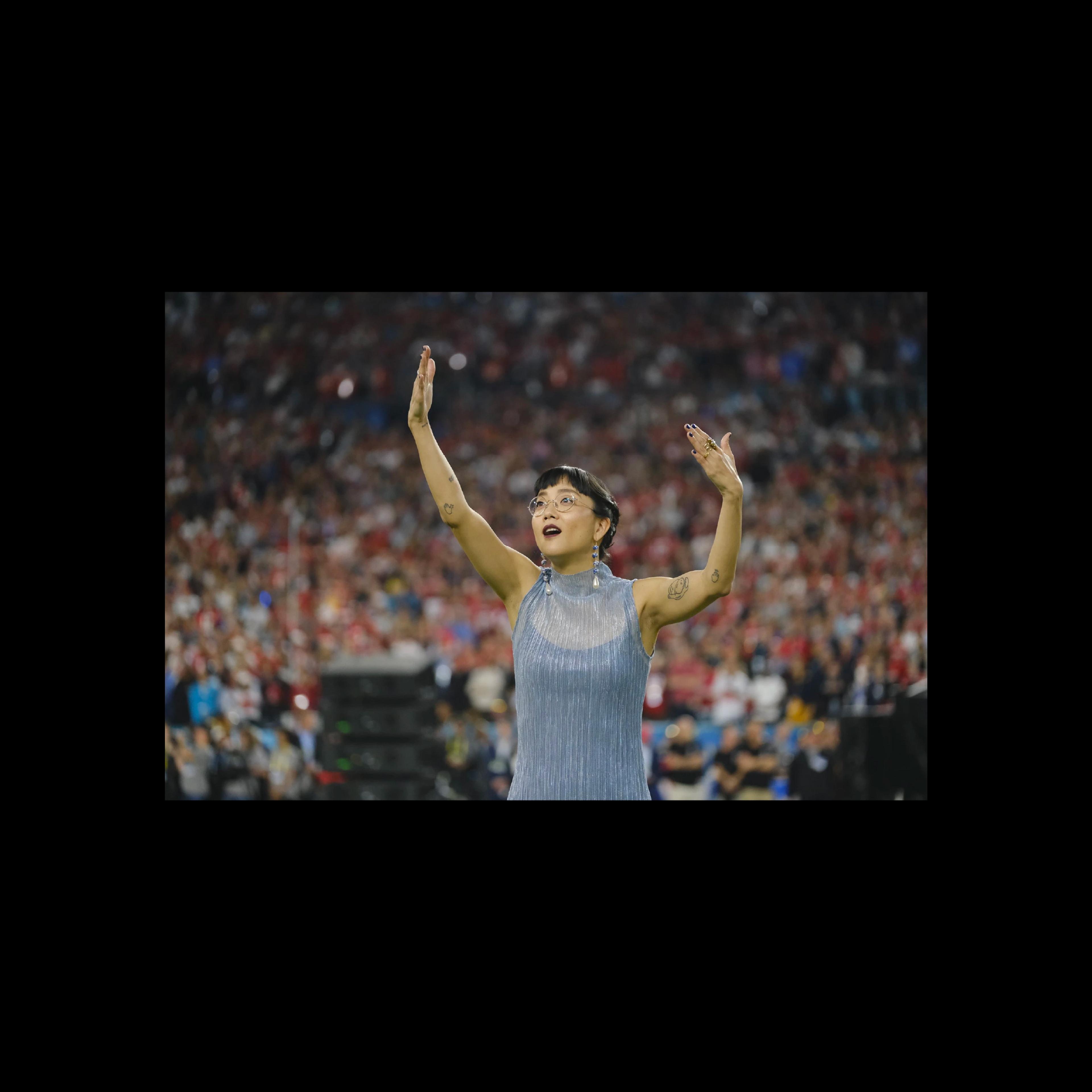 A performer signing with arms raised on the field of a packed stadium