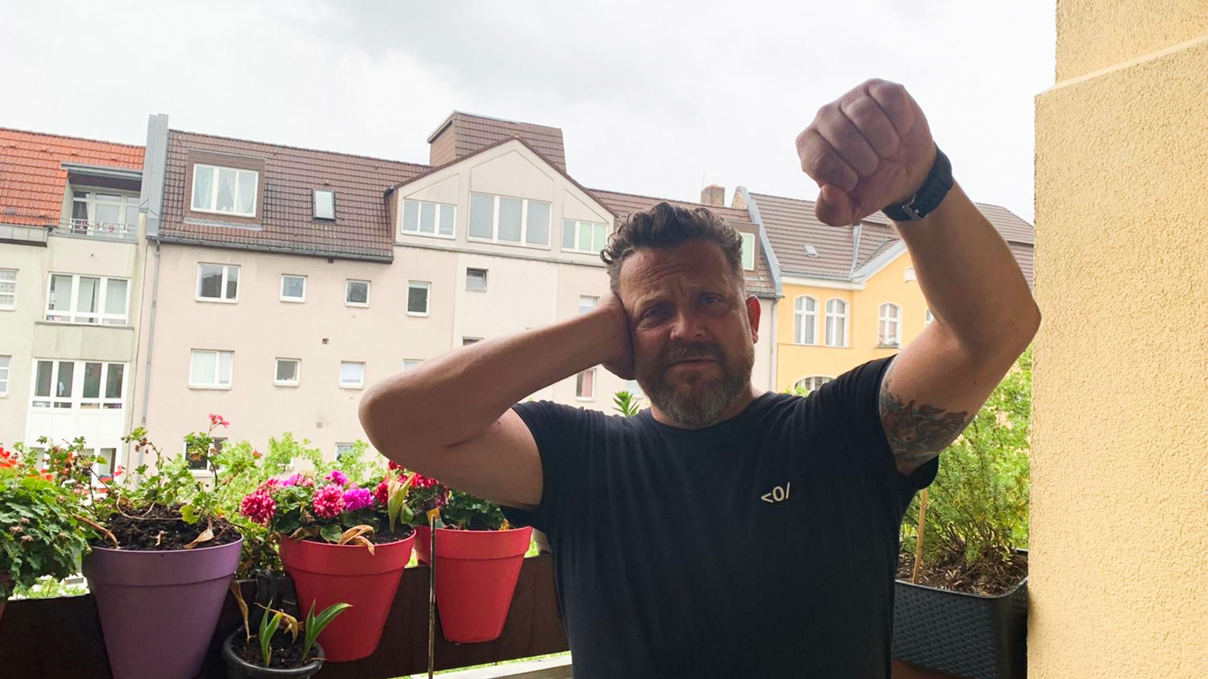 A man on a balcony with flower pots making the Deaf Power sign