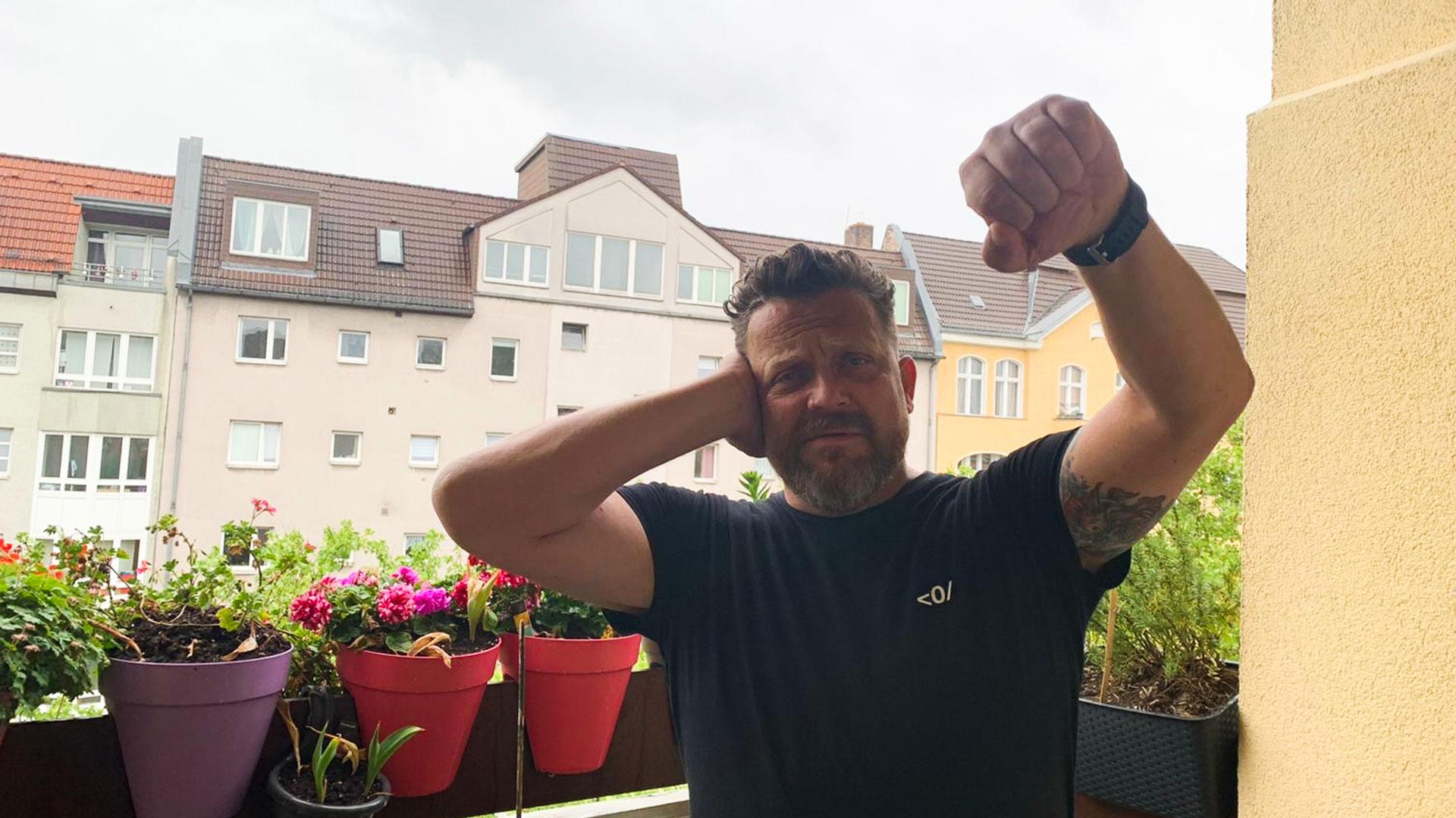 A man on a balcony with flower pots making the Deaf Power sign