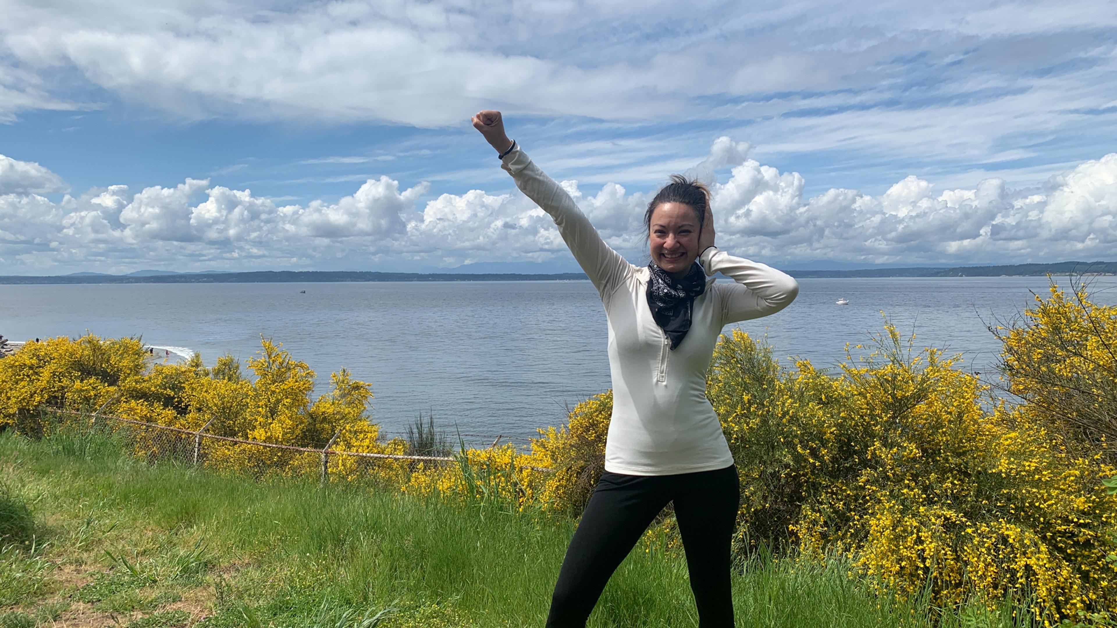 A woman on a grassy clifftop above the sea making the Deaf Power sign