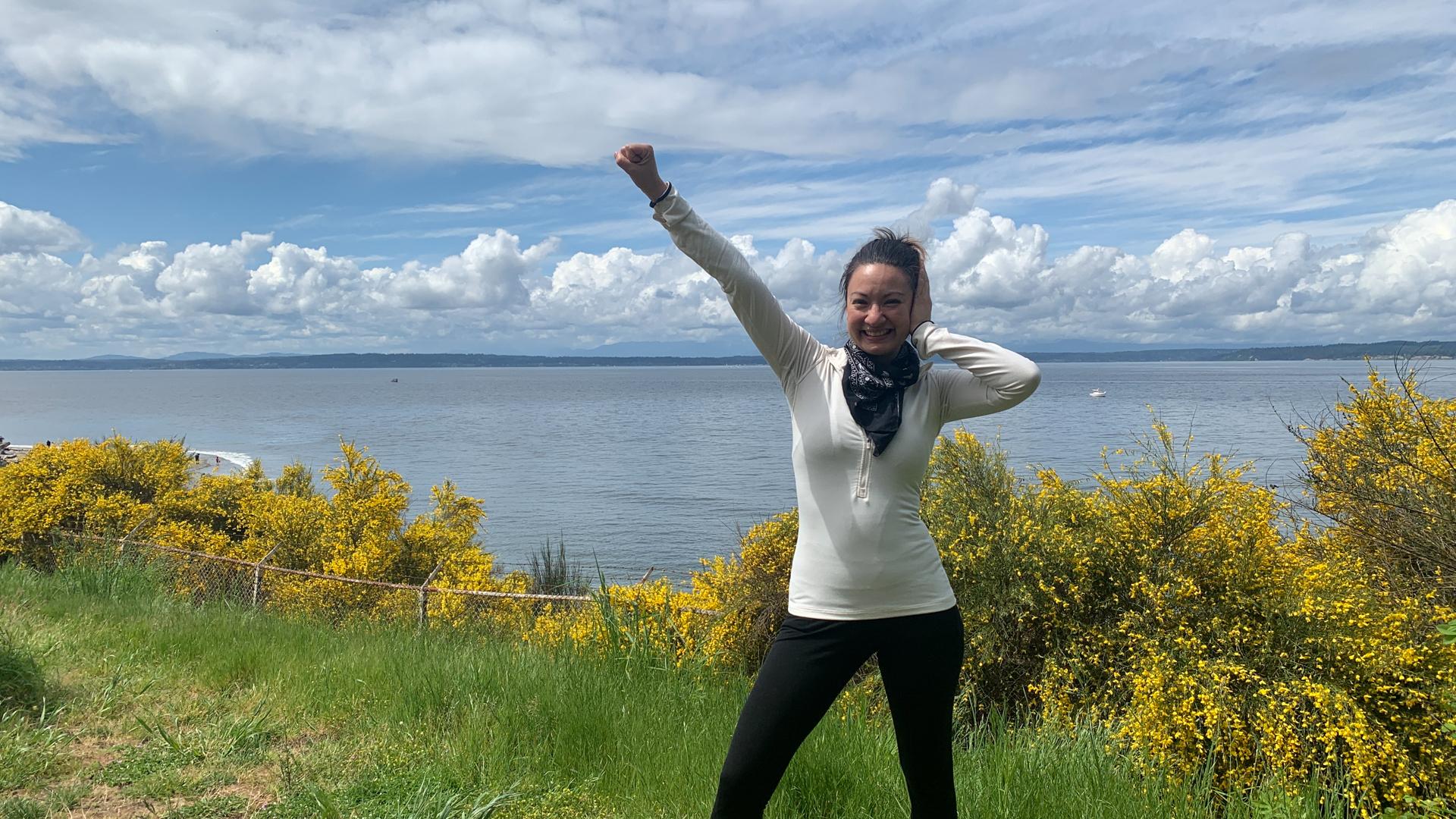 A woman on a grassy clifftop above the sea making the Deaf Power sign
