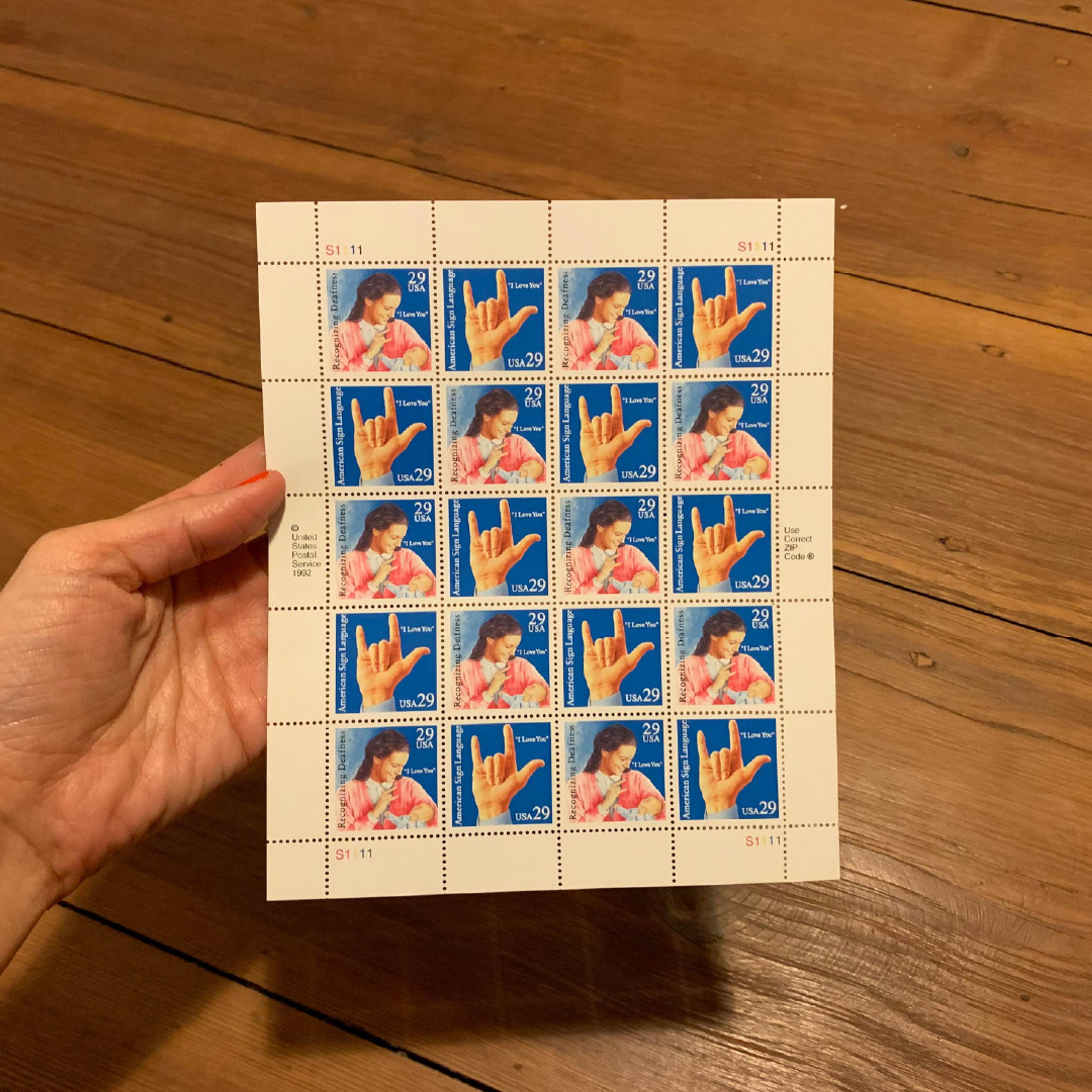 A hand holding a sheet of I-love-you postage stamps