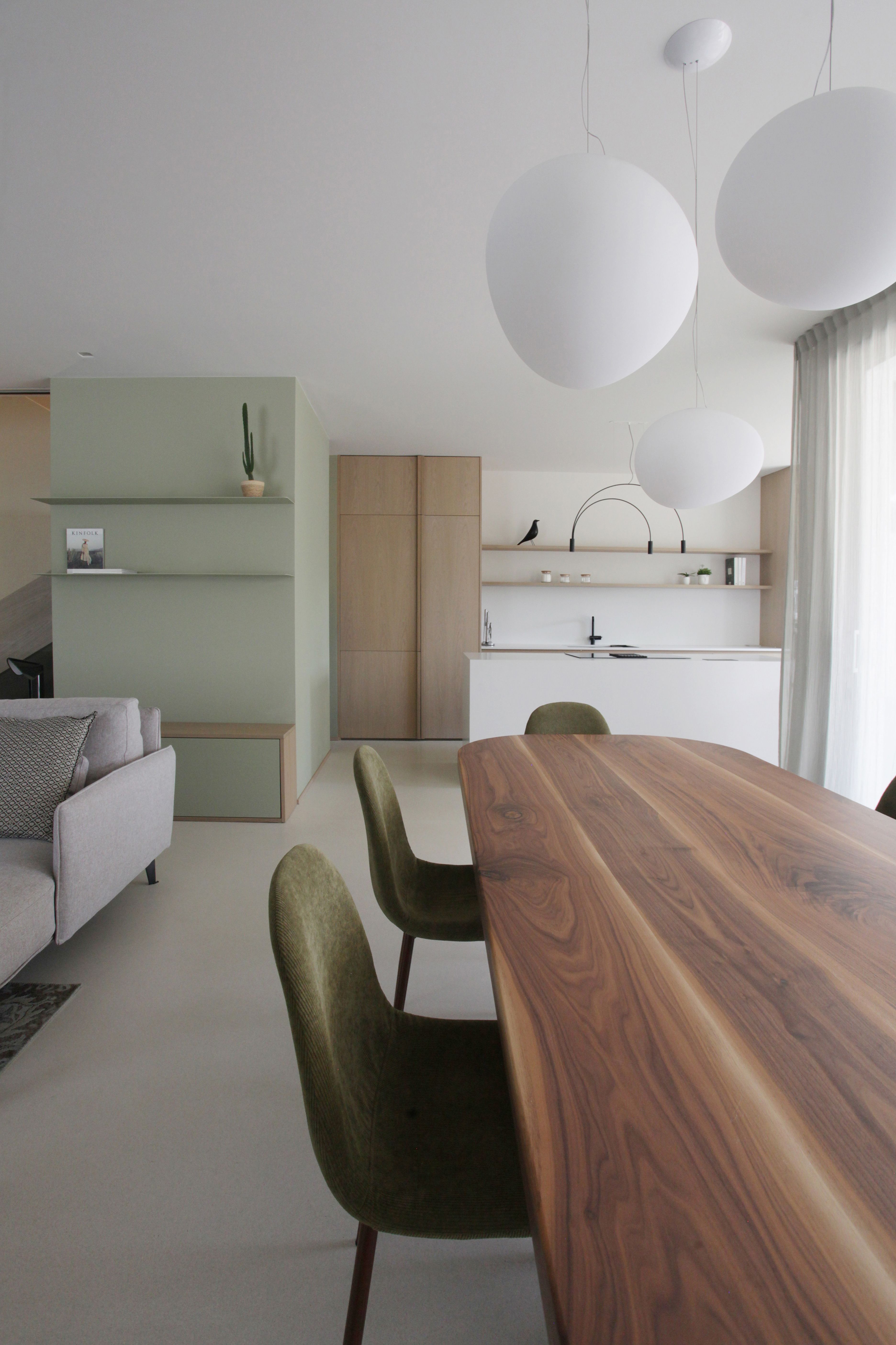 immagine a colori di una stanza con un tavolo di legno, delle sedie, delle lampade sospese a spera e uno scorcio di cucina