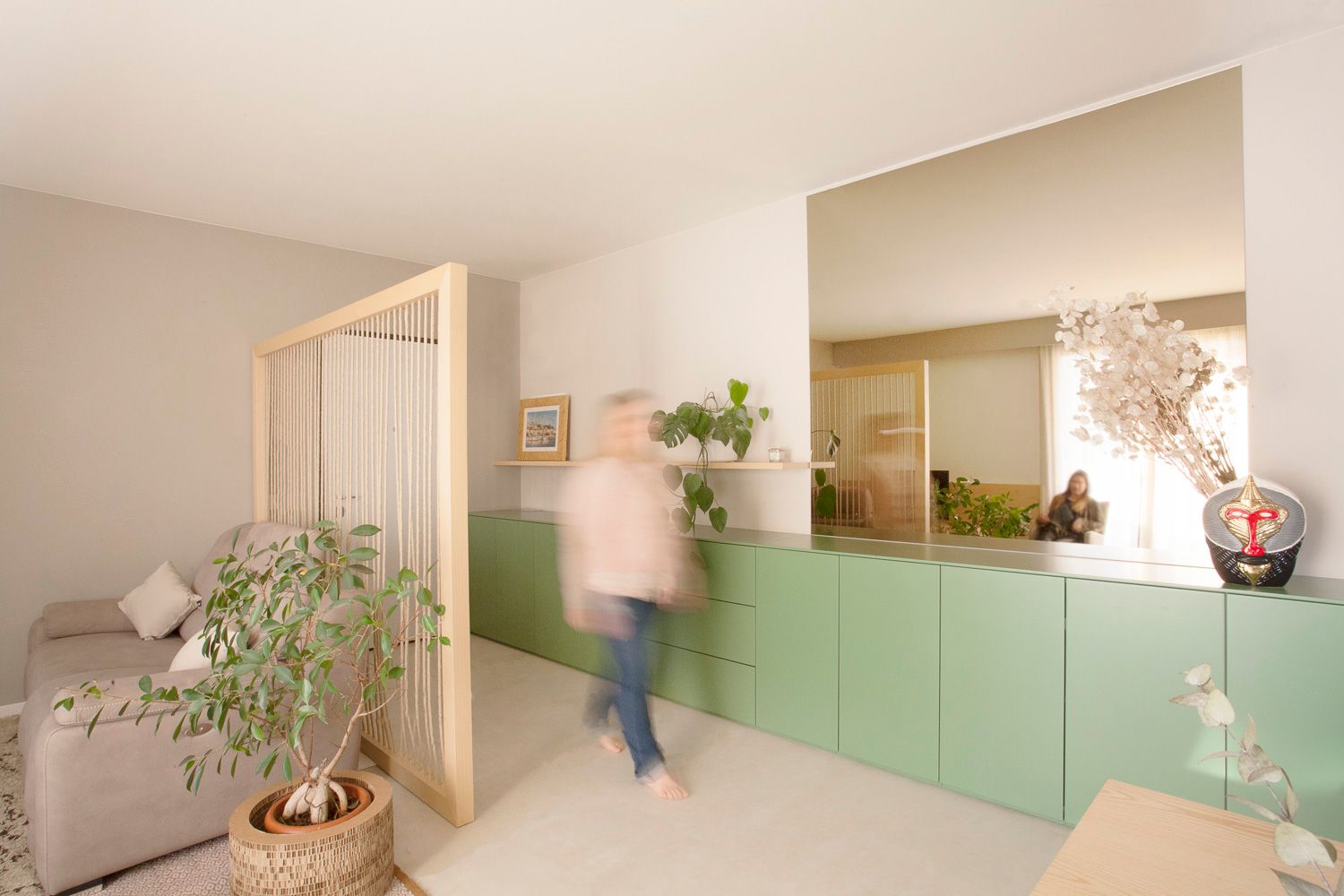 foto a colori con persona che passa davanti a una madia lunga verde con ampio specchio 