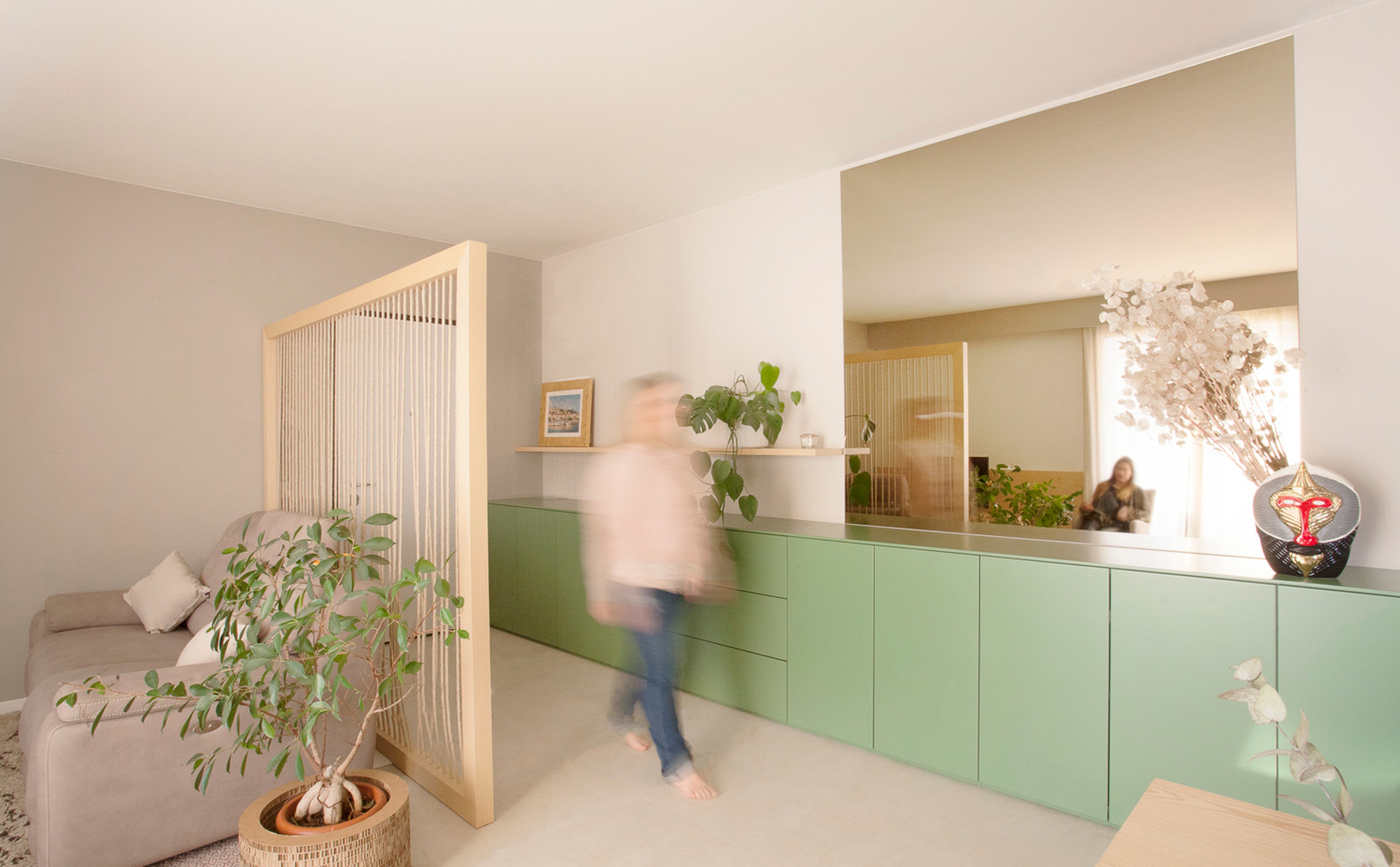 foto a colori con persona che passa davanti a una madia lunga verde con ampio specchio