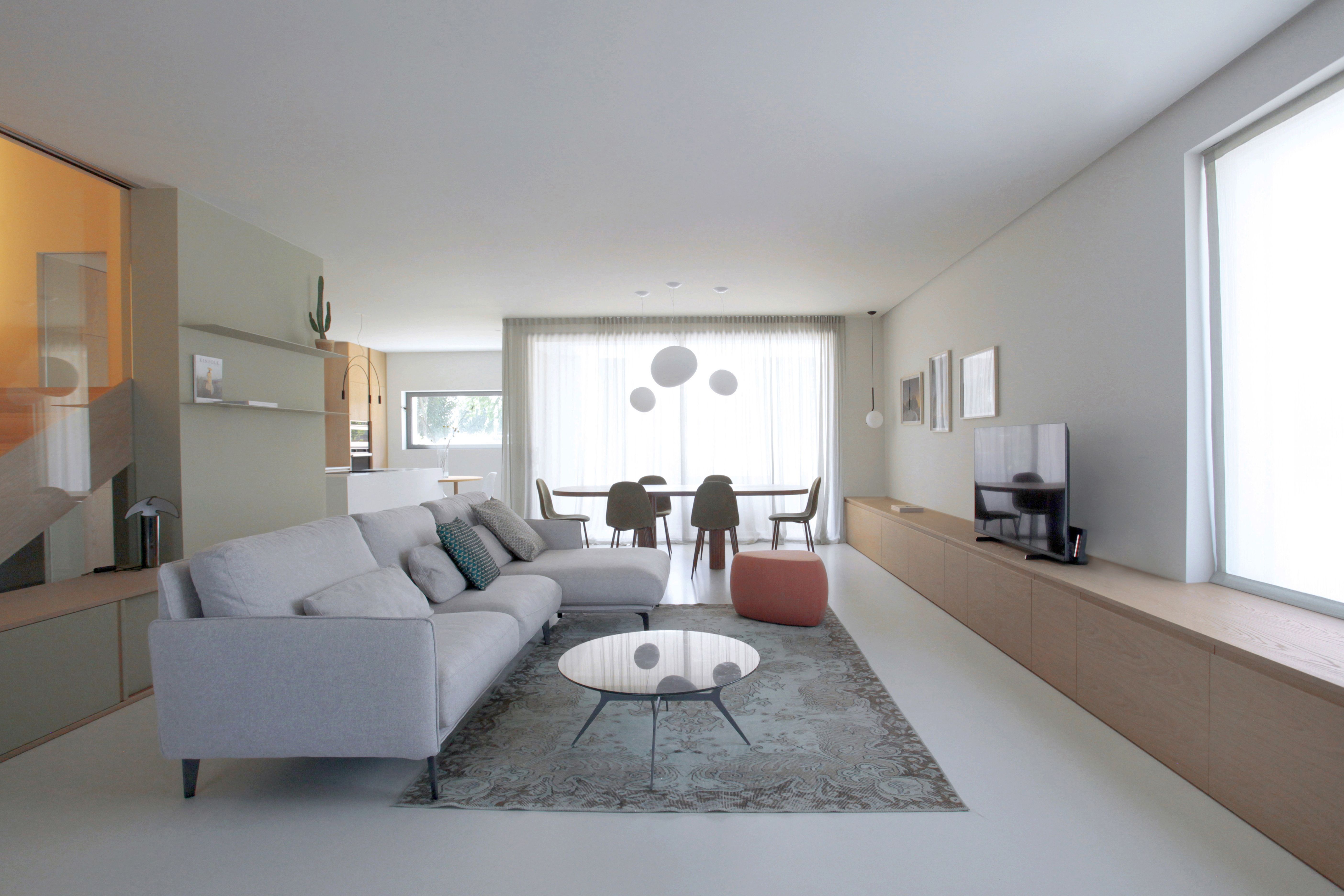 Foto a colori di un living composto da divano, tappeto, mobile tv in rovere e ampie vetrate.