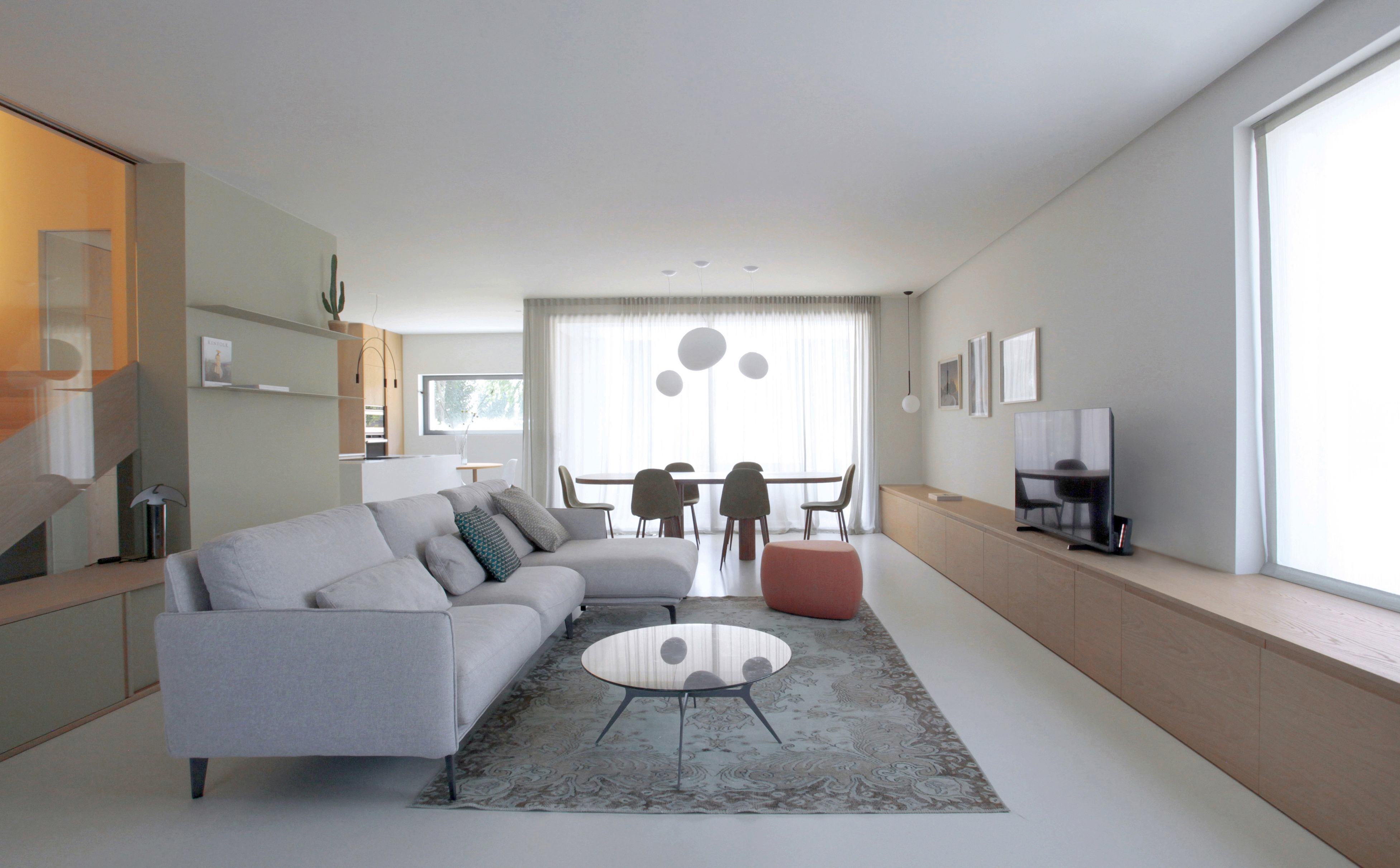 Foto a colori di un living composto da divano, tappeto, mobile tv in rovere e ampie vetrate.