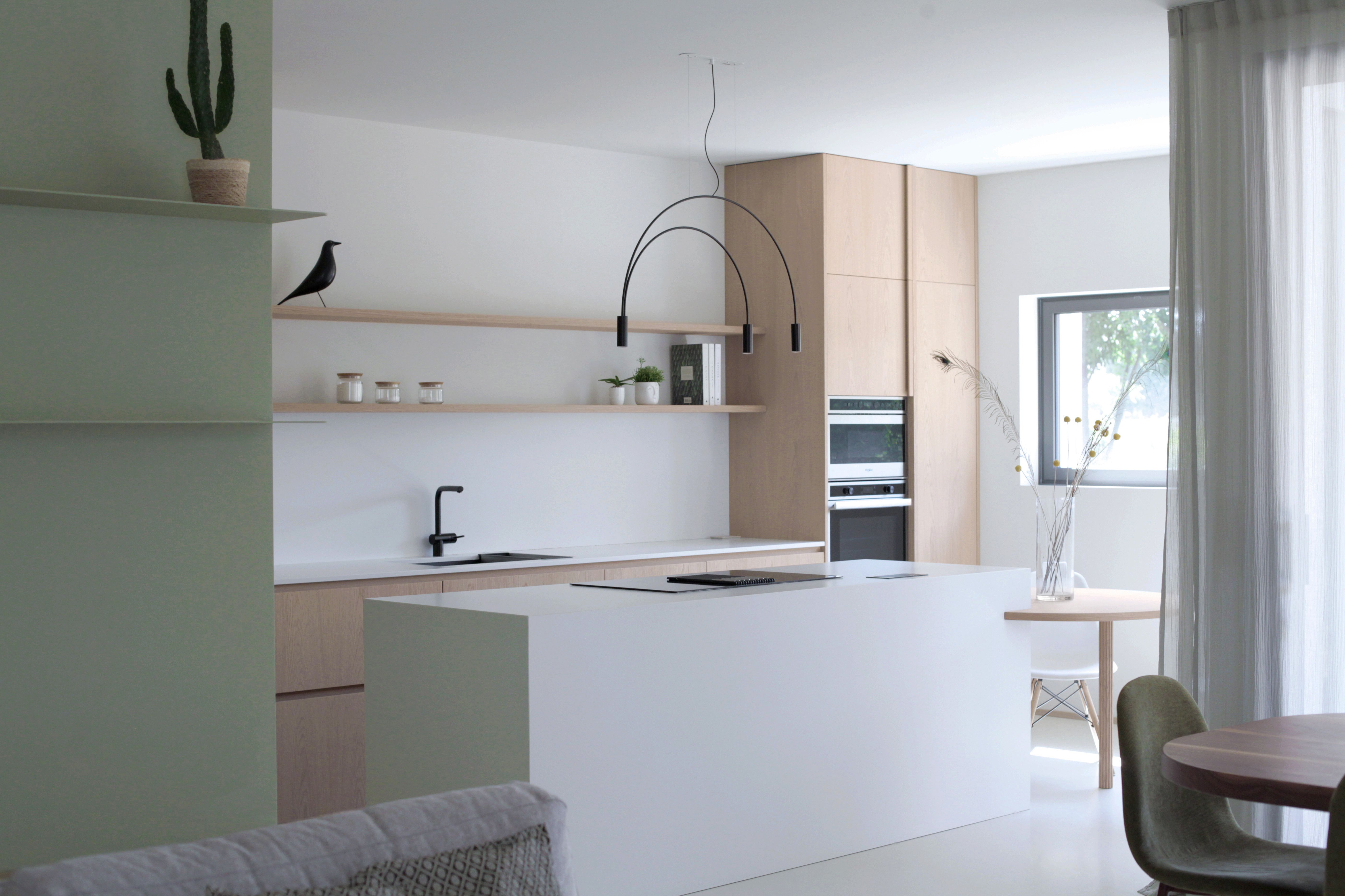 Foto a colori. Cucina luminosa con ampia isola, colore rovere e bianco. Parete verde salvia.