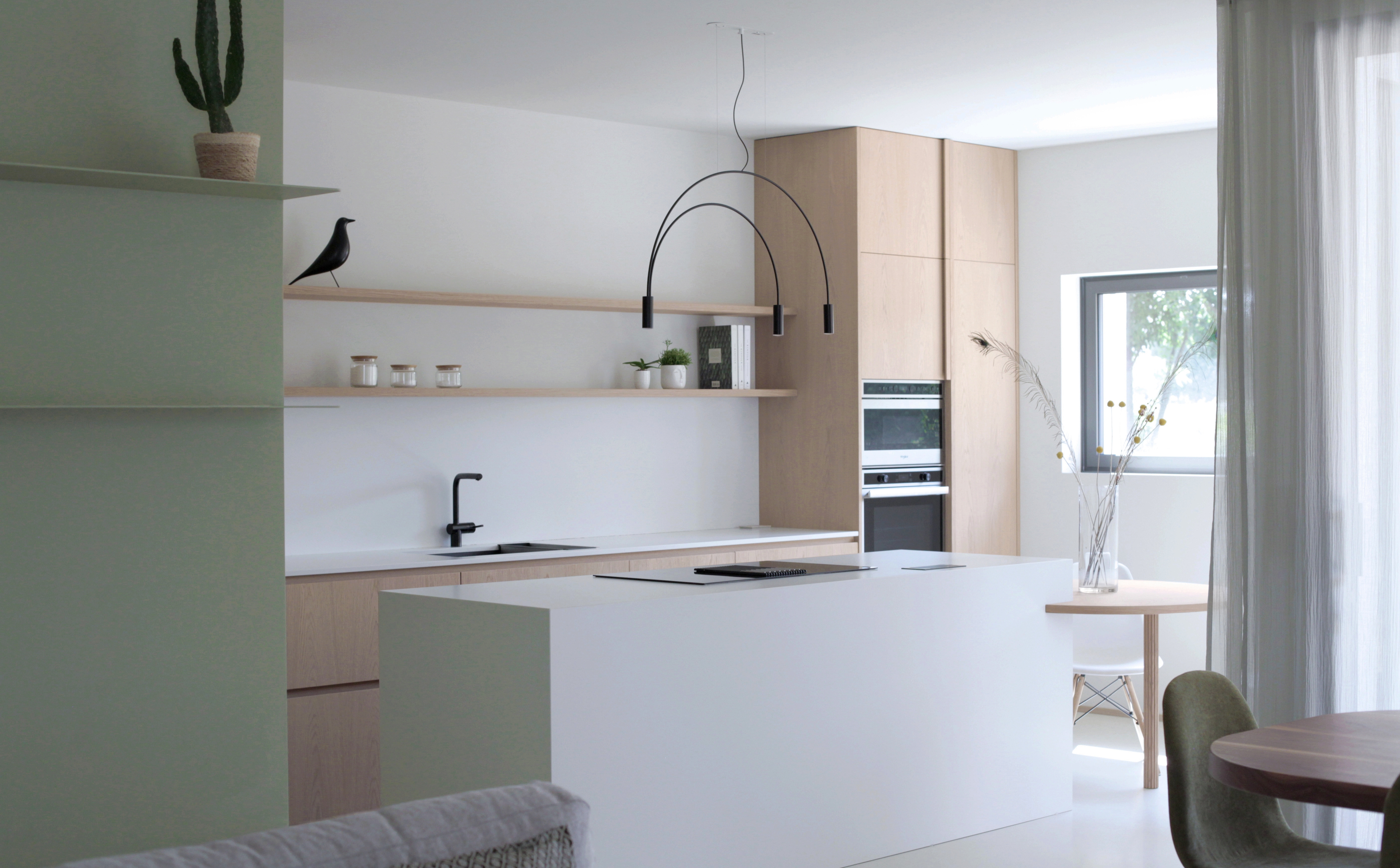 Foto a colori. Cucina luminosa con ampia isola, colore rovere e bianco. Parete verde salvia.