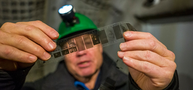 A man holding a piqlFilm strip inside a cave.